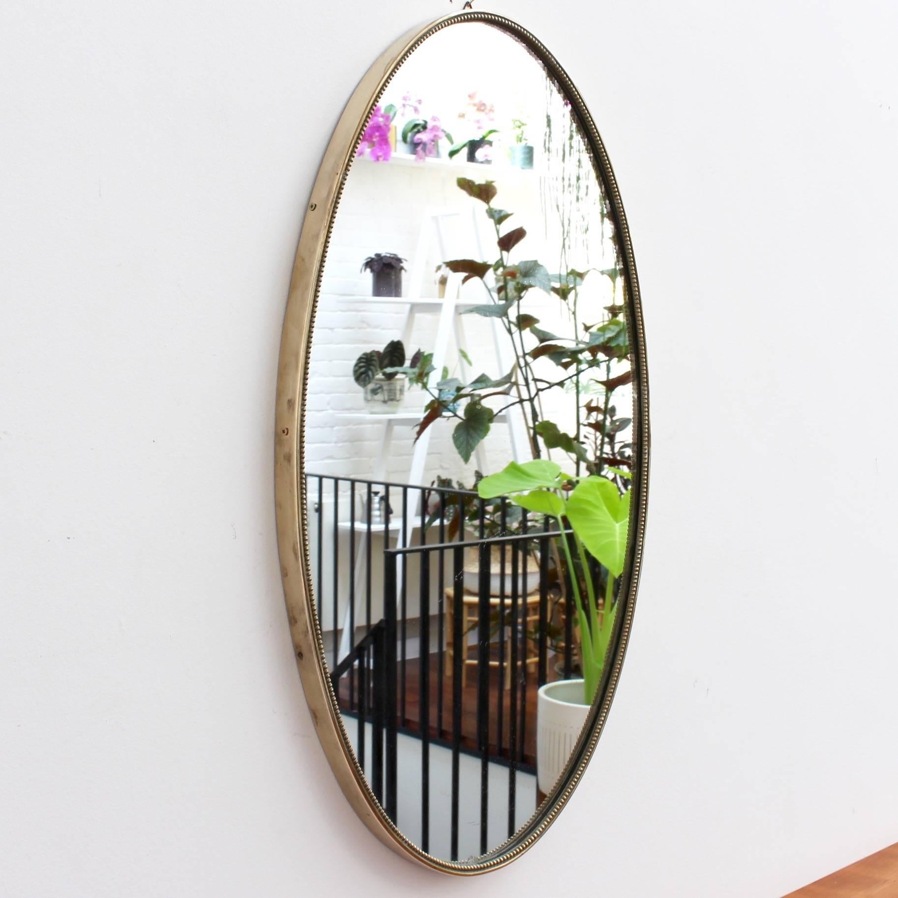 Oblong Italian wall mirror with brass frame, circa 1950s. The mirror is beautifully oblong-shaped with a distinctive beaded detailing. Always elegant and distinctive in a modern Gio Ponti style. This mirror is in very good vintage condition. There