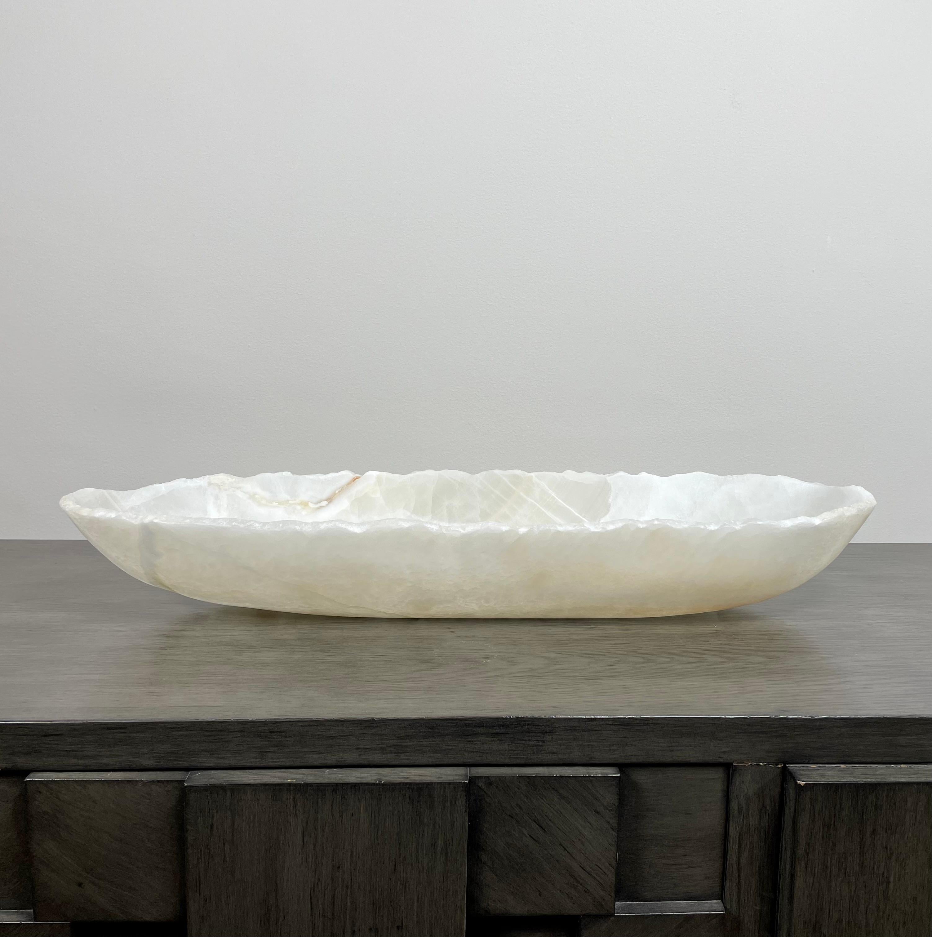 An elegant oblong medium onyx bowl. It has serene tones of white and off white with some veining in earth tones. This one of a kind decorative vessel is meticulously hand-carved from a single piece of onyx by skilled artists to reveal its' inherent