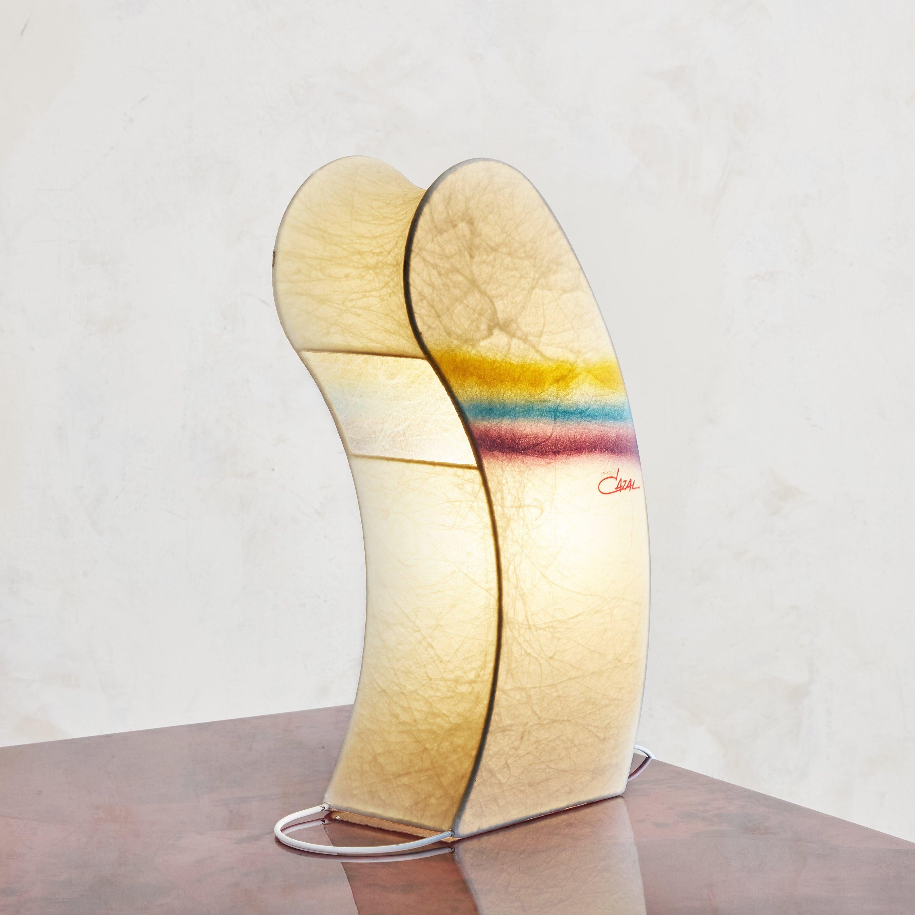 Lámpara de sobremesa italiana con forma de capullo arco iris de los años 70, diseñada por Cazal Crèation. Esta juguetona lámpara está compuesta de pergamino blanquecino con detalles de rayas horizontales, que pasan por un degradado de tonos