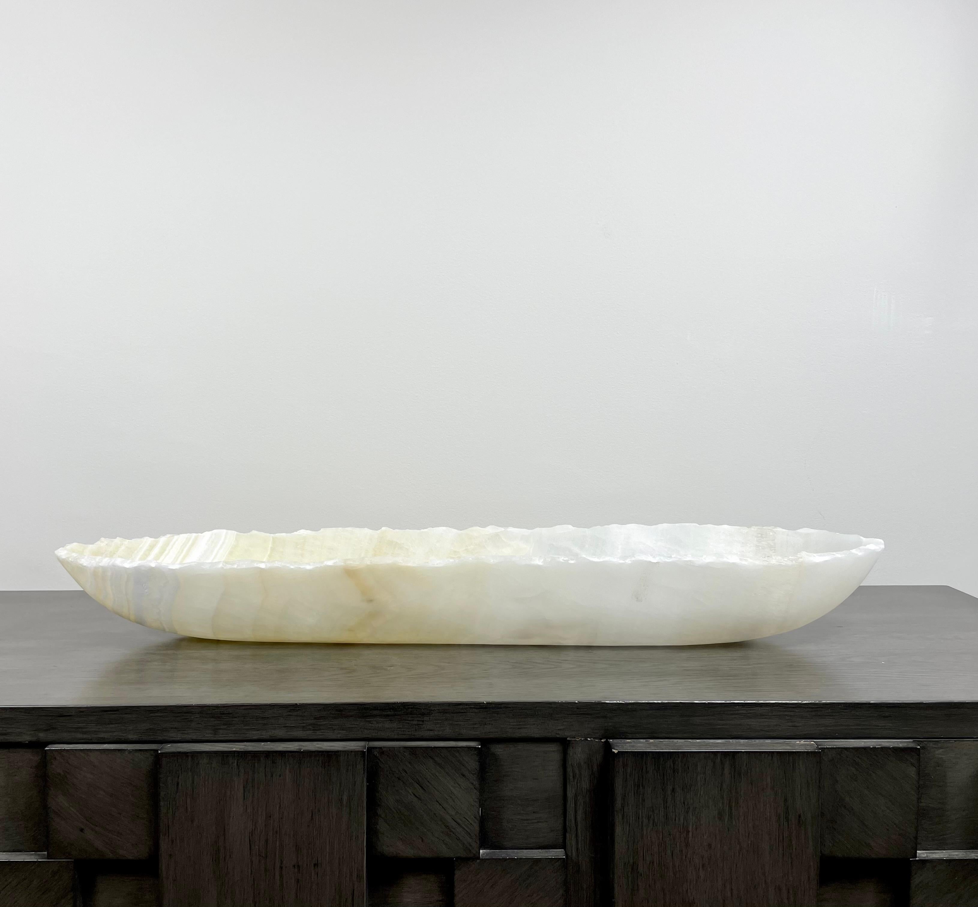 An elegant oblong large onyx bowl with stunning striations. It has serene tones of cream, pale yellow and white. This one of a kind decorative vessel is meticulously hand-carved from a single piece of onyx by skilled artists to reveal its' inherent