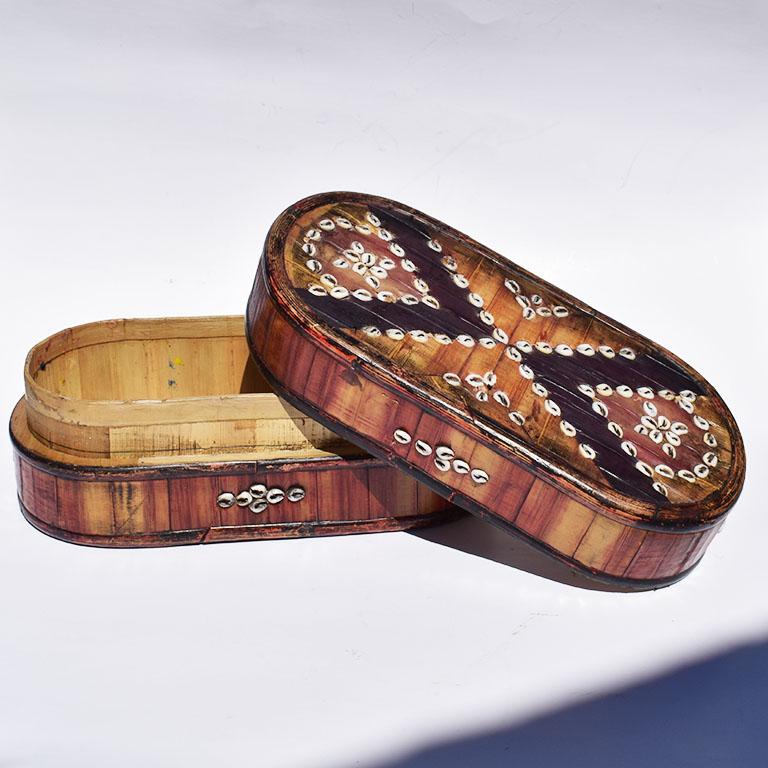 Oblong wooden box with inlaid shells. Created from bamboo or other similar material, this decorative box features white seashells in a tribal black and white design. At the top, black geometric lines are accented with white inlaid seashells. Similar