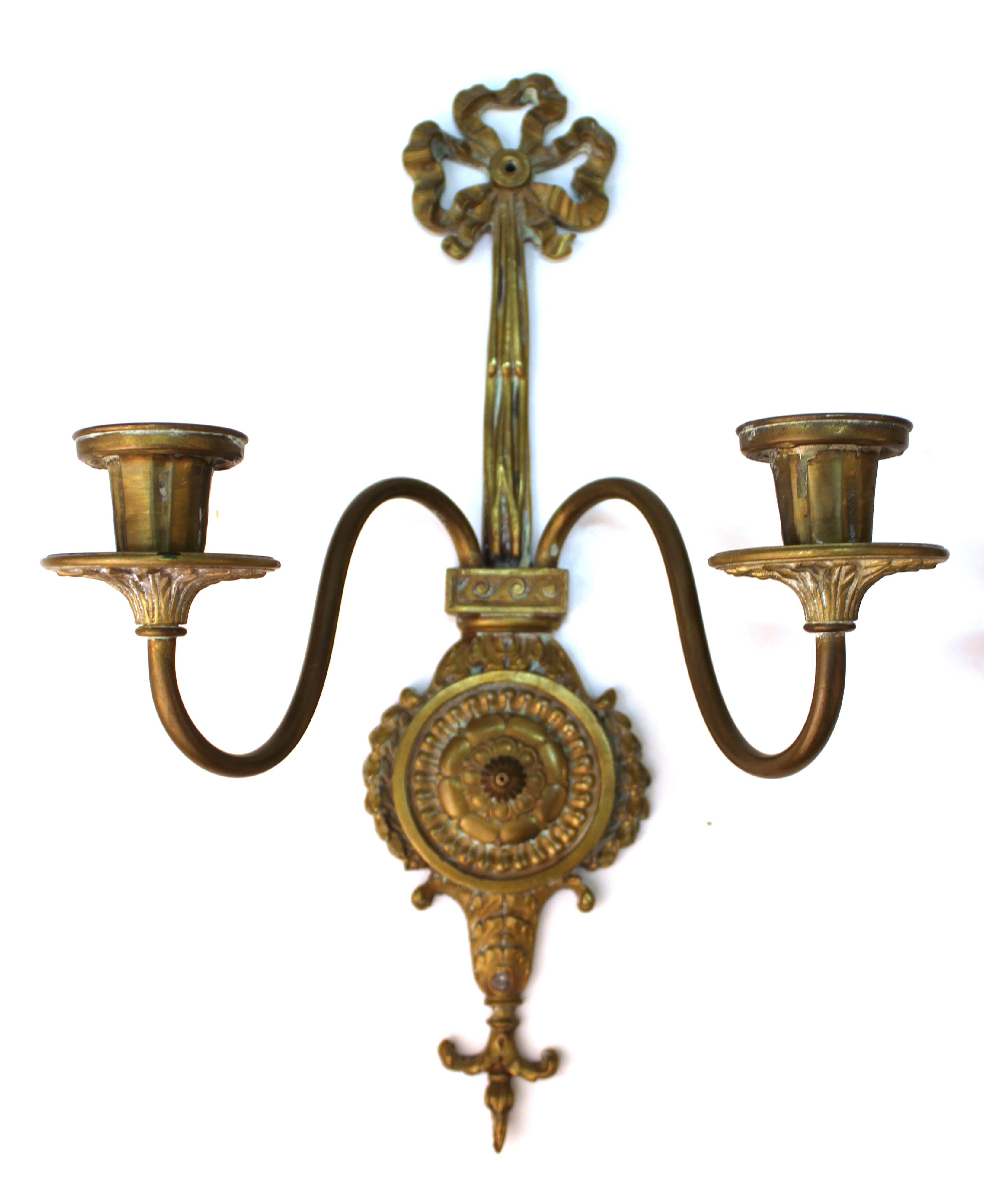 O.C. White Company American neoclassical style pair of gilt brass candelabra wall sconces, dating from the 1920s and cast in ribbons, rosettes and leaves. The backs have factory stamps 