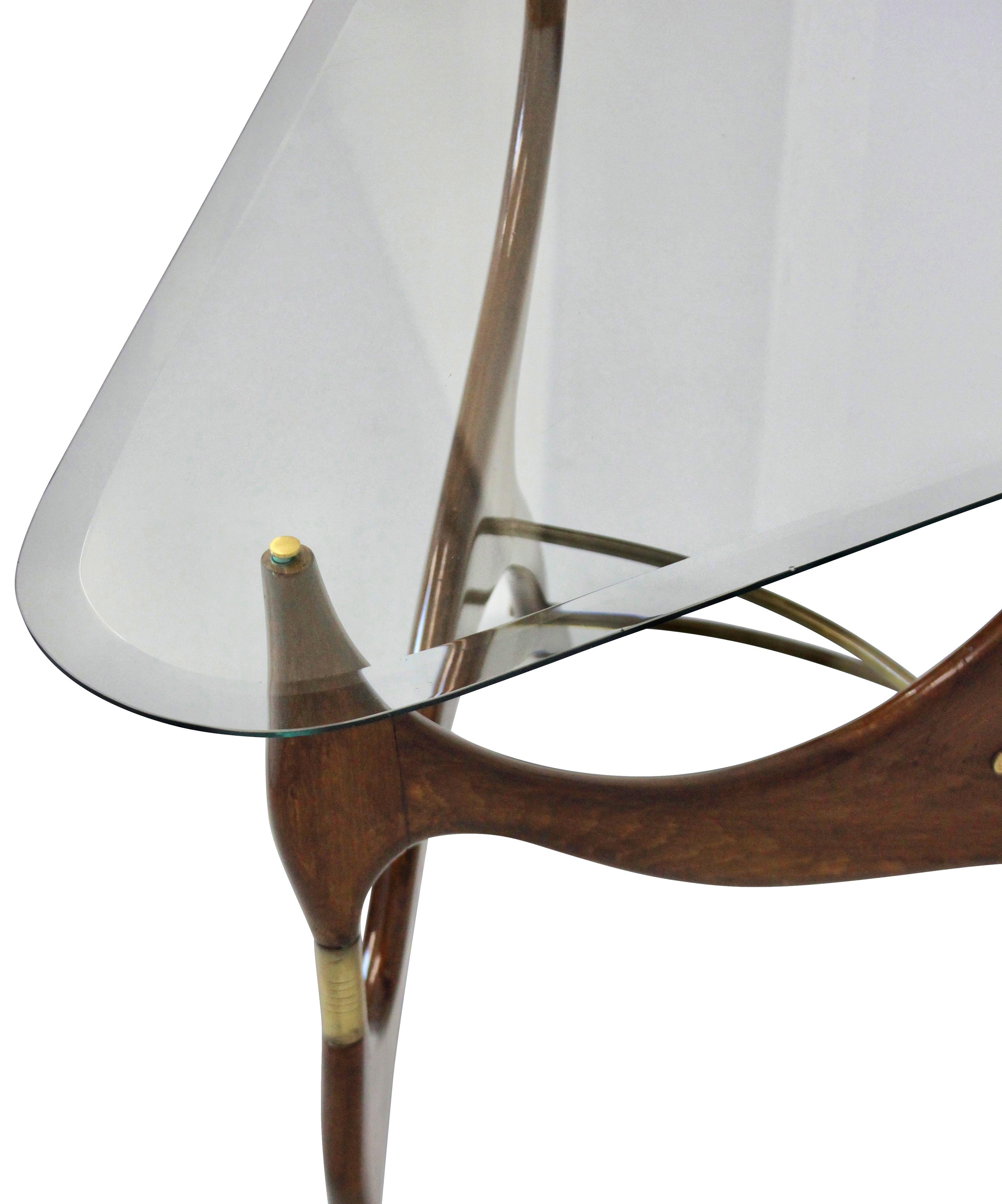 An unusually sculpted occasional table in the manner of Carlo Molino. In fruitwood with brass detail and a glass top.

 