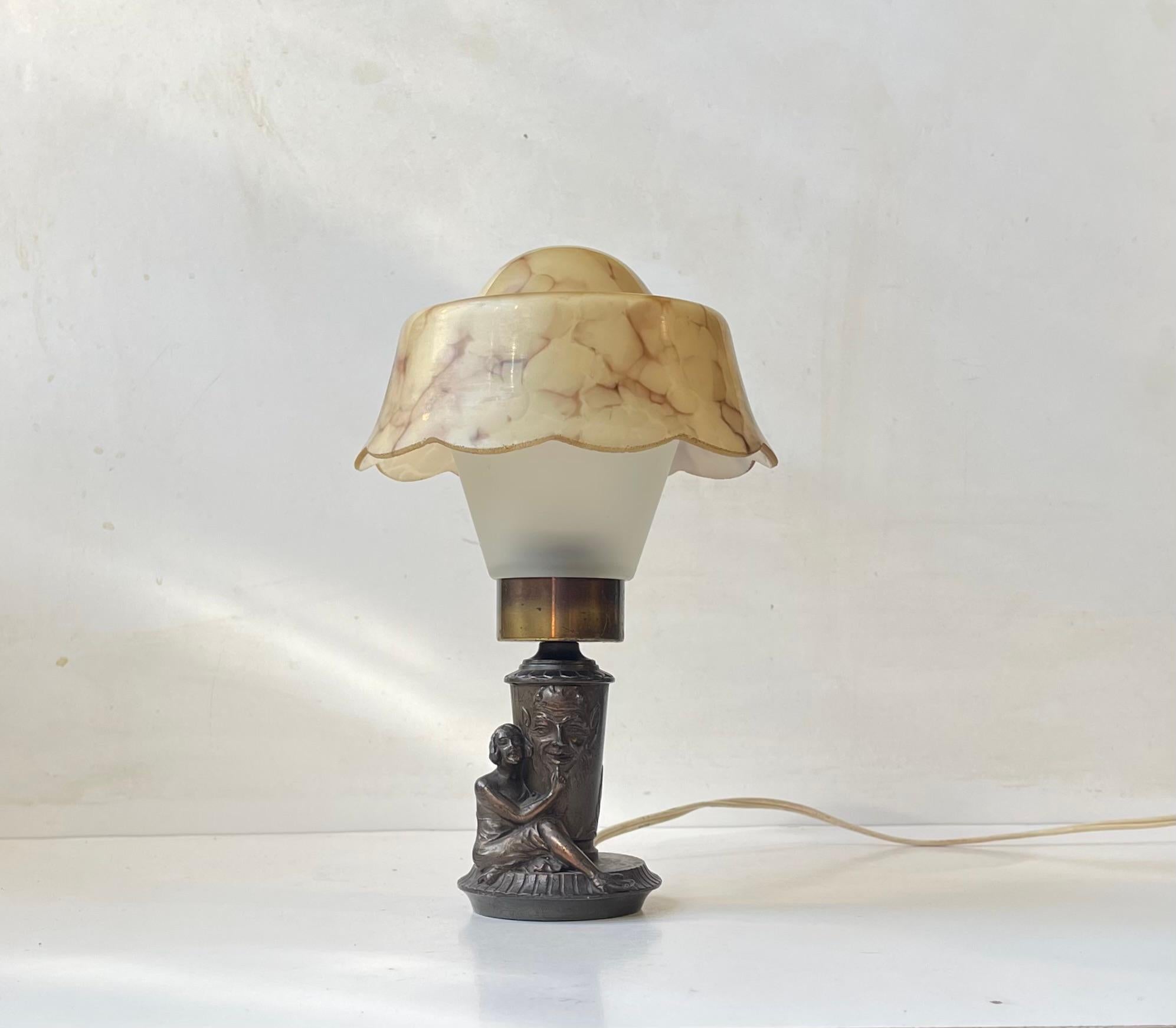 You do not come across these type of objects very often. The occult or satanic themes are mostly a very modern materialized phenomenon. However this small sculpted bronzed metal table light mounted with 1930s marble glass shading was made by an