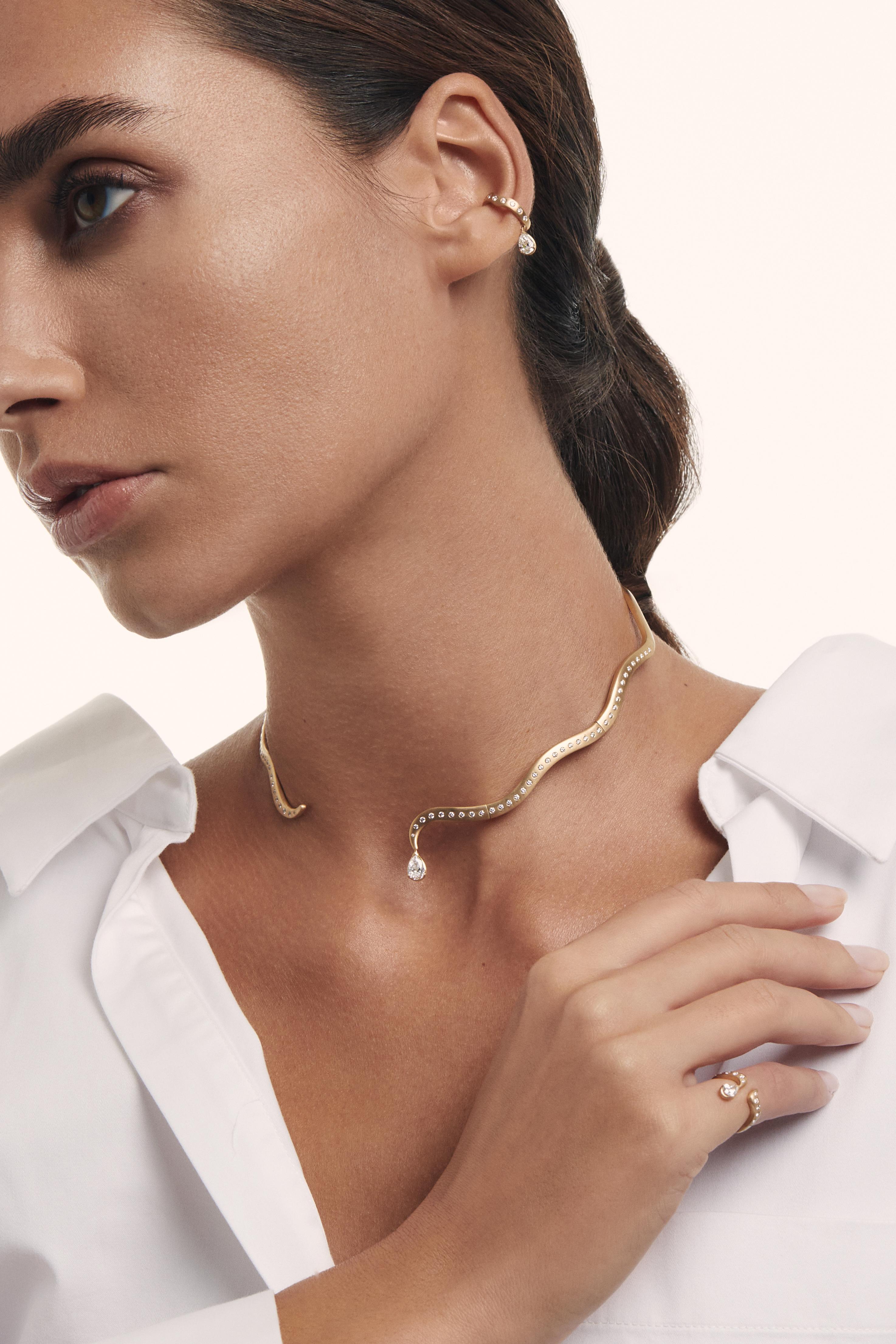 The Ocean Drop Diamond Choker is a contemporary interpretation of timeless design. It is crafted in 18K matte gold and features a single pear cut diamond in a floating drop setting that moves gently with the wearer. Each round diamond along the