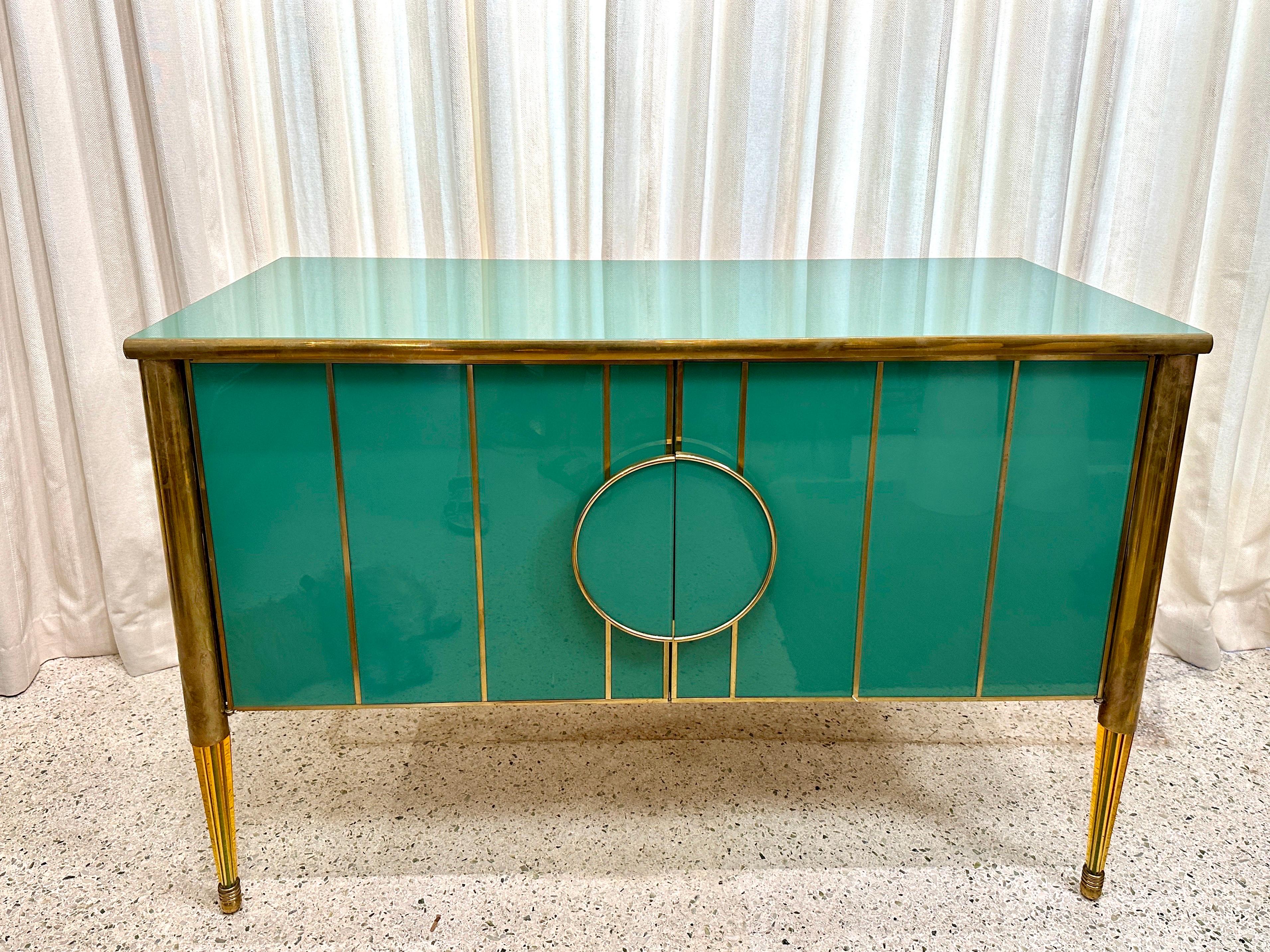This amazingly crafted 2-door cabinet clad completely in Murano green glass and trimmed with brass, also features wonderful tapering glass legs.  Interior long clear glass shelf.  NOTE:  TWO (2) available, sold separately.  THIS ITEM IS LOCATED AND