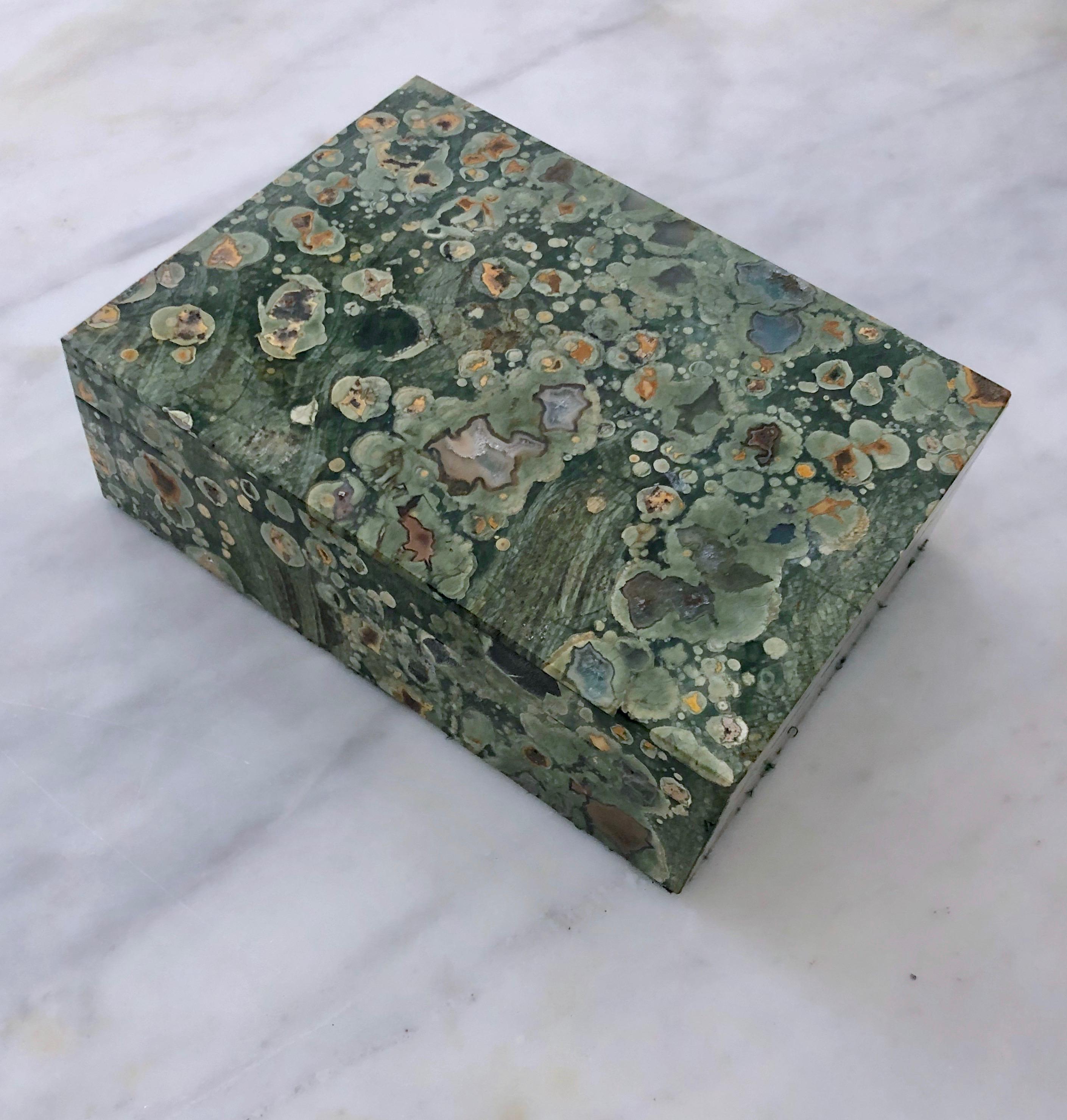 This box is made of a stone called 'Ocean Jasper' or orbicular jasper originating from Madagascar. It has beautiful spherical patterns with quartz druzy inclusions. The box has a brass hinge and is lined with green felt in what appears to be unused
