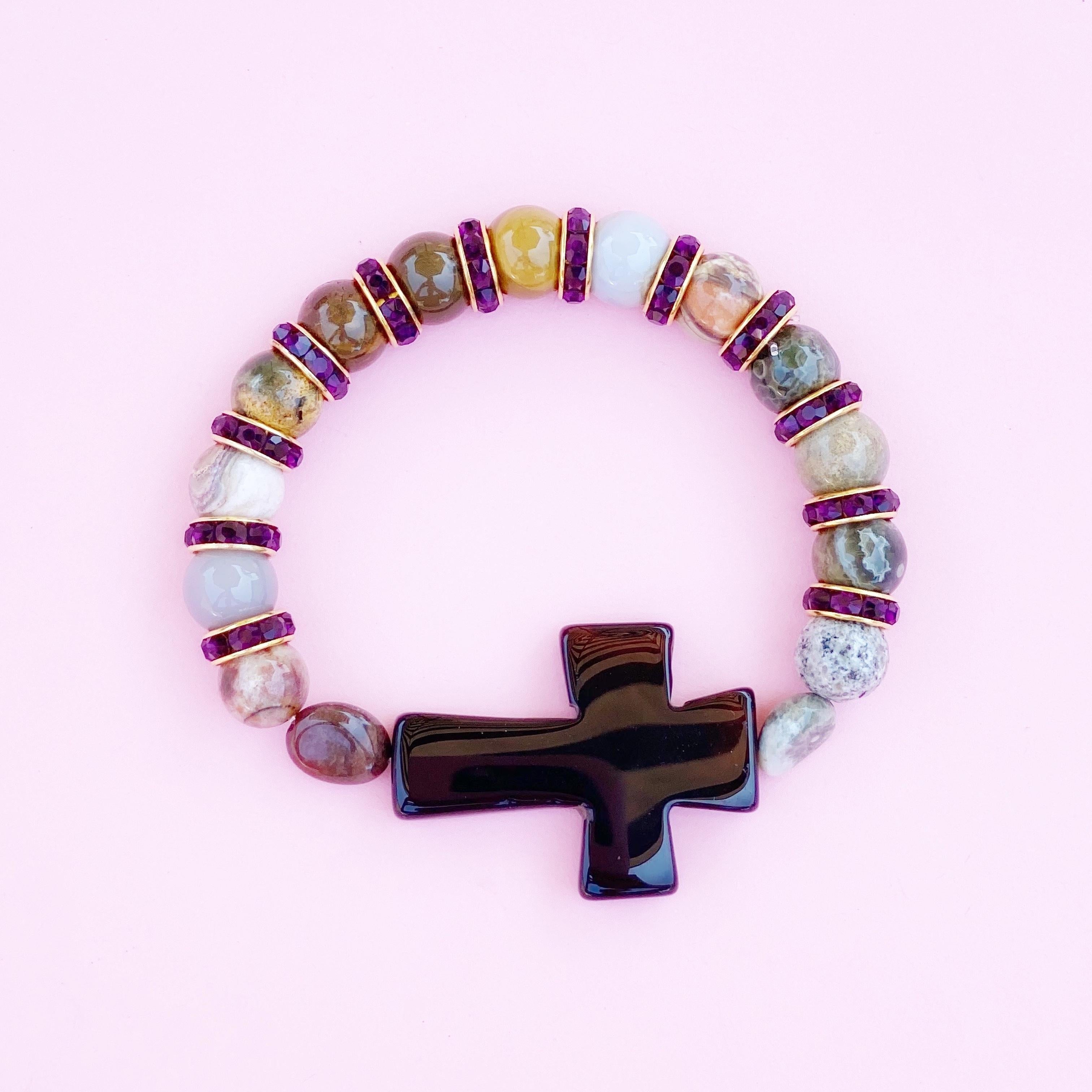 10mm polished Ocean Jasper gemstones with black Onyx gemstone cross flanked by Amethyst-colored crystal rhinestones and gold-plated accents. 

Stretchy elastic band, one size fits most.

Due to the uniqueness of natural gemstones, each stone will