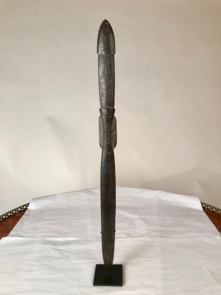 A Papua New Guinea hand carved ebony lime spatula covered with continuous swirl designs etched on the open handle and shaft, with some traces of lime still present. Mounted on a custom steel base, this tribal artifact from the Massim people is also