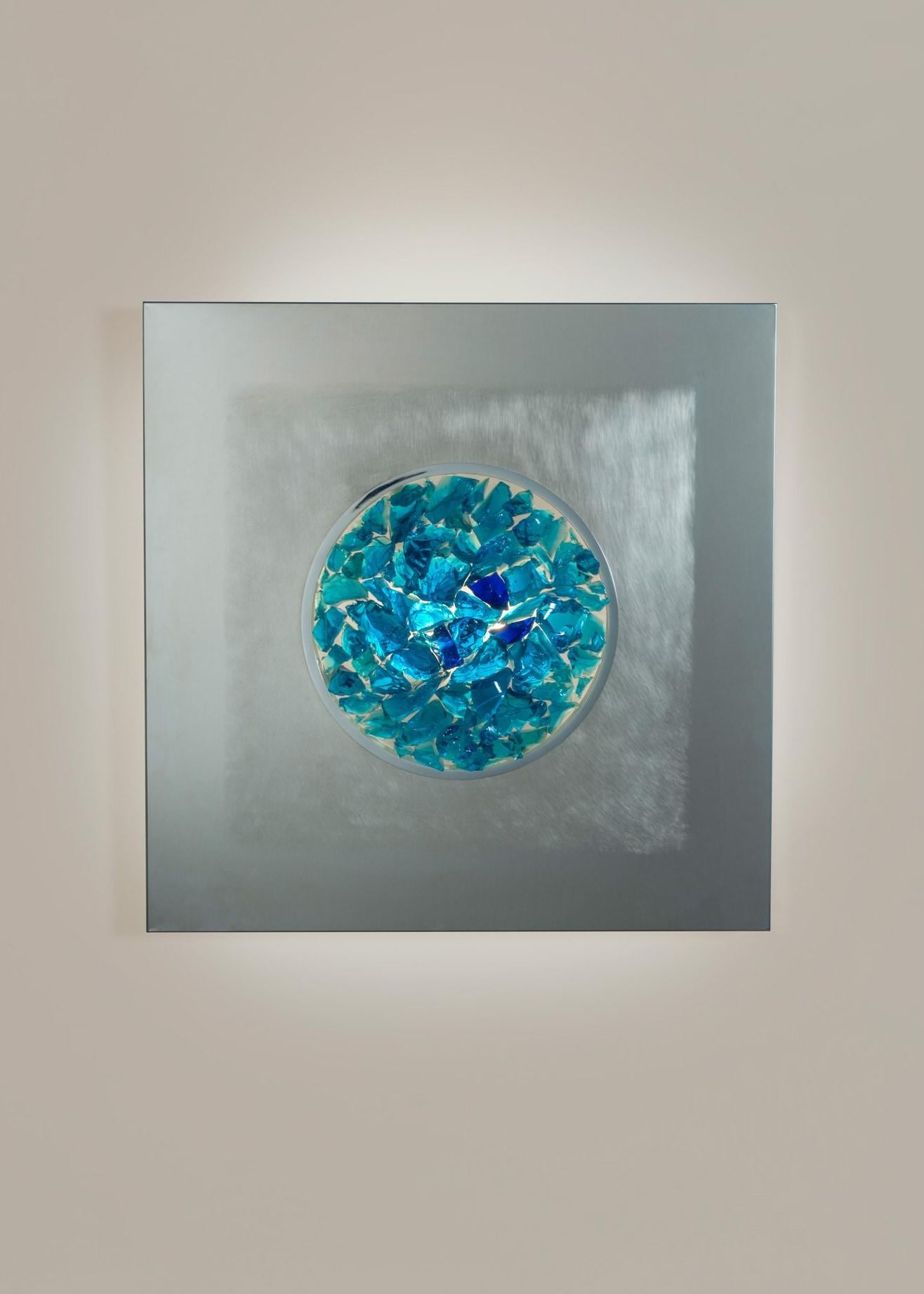 Luminous wall sculpture composed of a box element in polished and satin stainless steel. Arranged in the center irregular elements in Murano glass in shades of blue.
