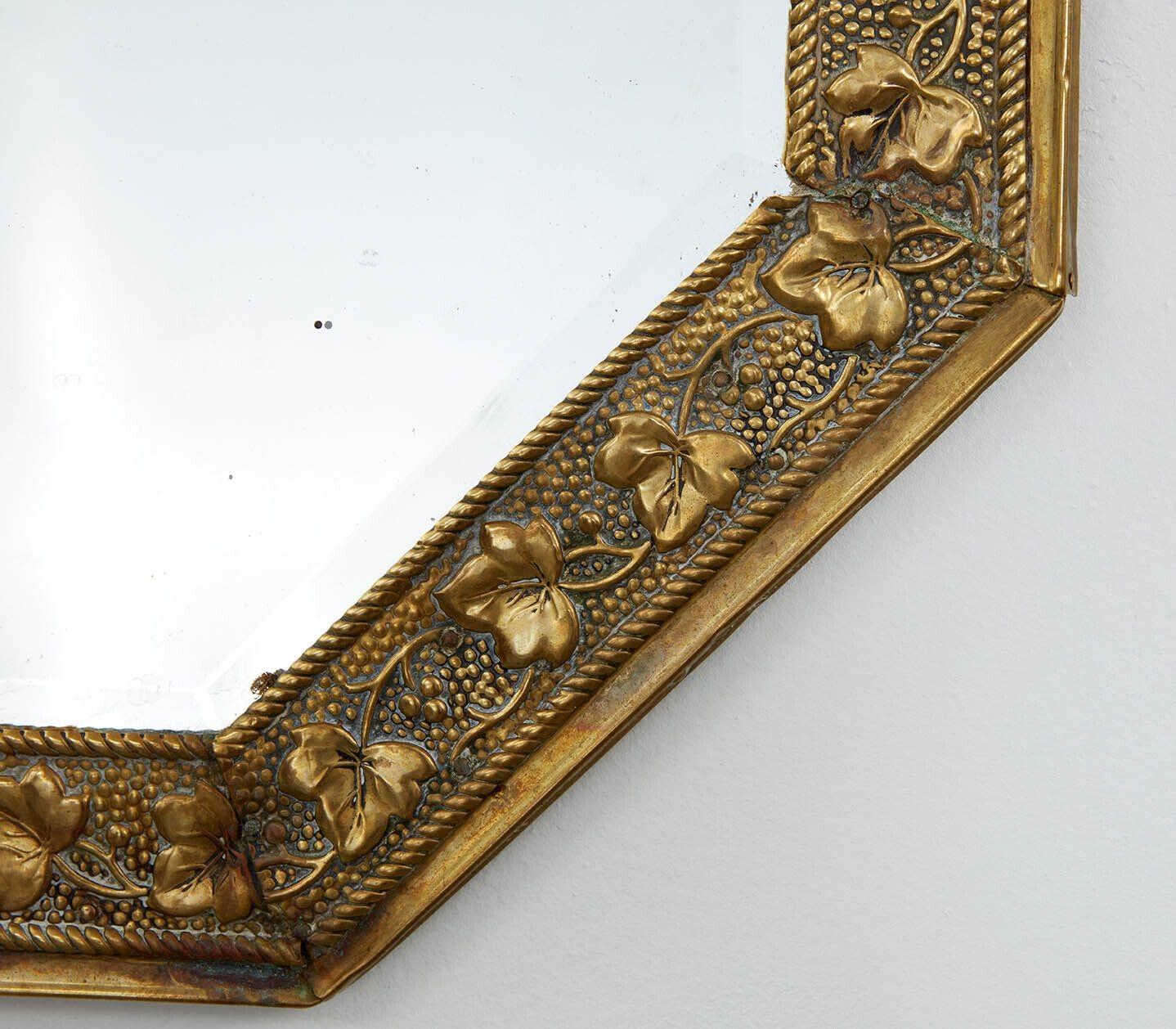 Un miroir Art & Crafts de forme octogonale avec une décoration de feuilles de vigne et de raisin sur un fond de broche en relief, conservant le verre biseauté et le panneau arrière d'origine.