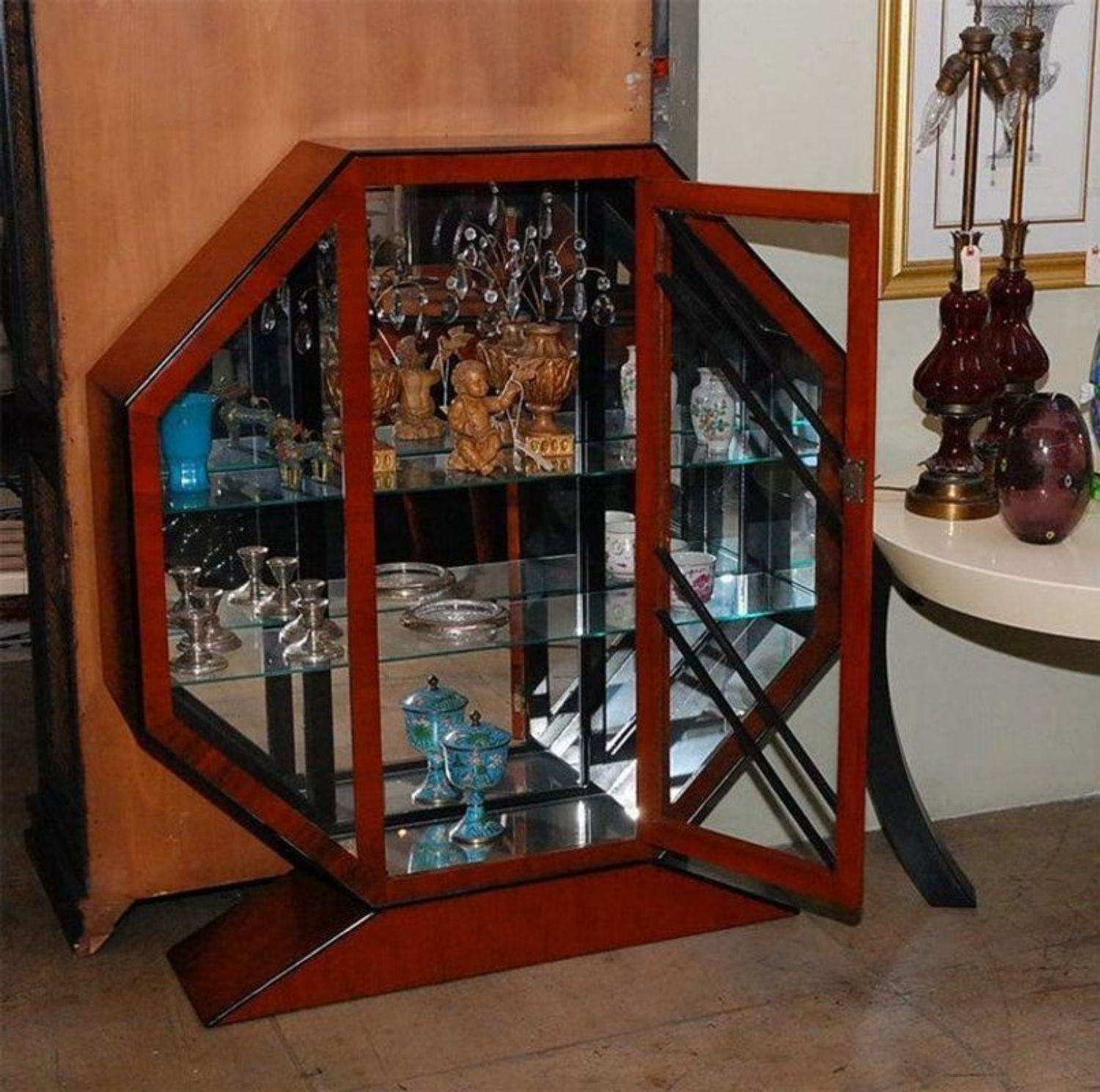 Octagonal cherry vitrine with ebonized wood. Mirrored interior, three glass shelves and center door. Mounted on a triangular base.