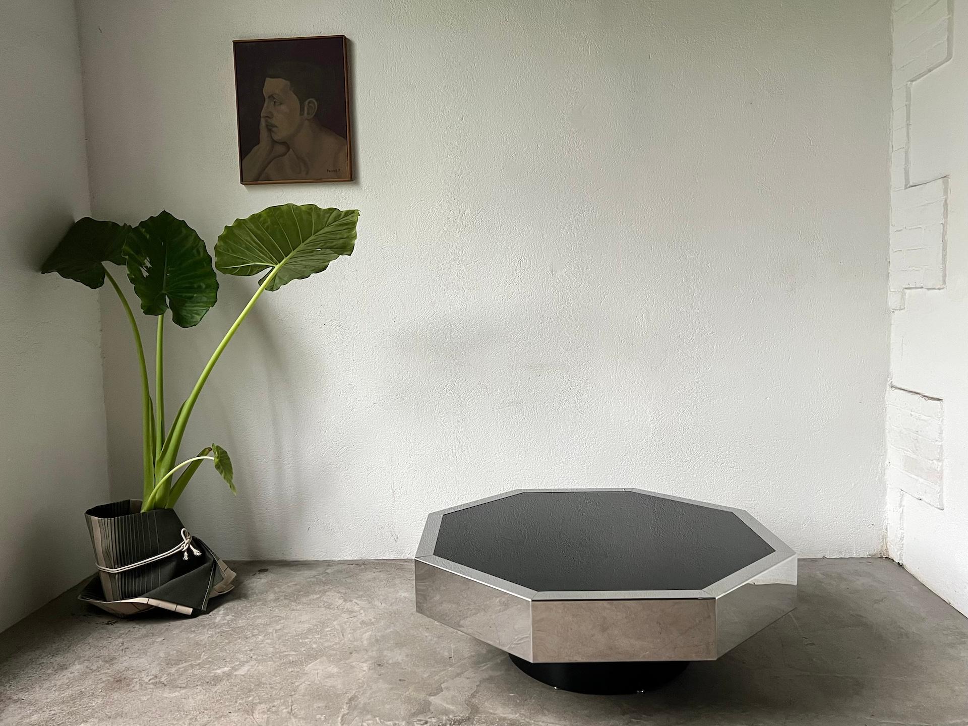 Coffee table from the 80s attributed to Willy Rizzo. In brushed stainless steel and with a black glass top. A futuristic and modern design. The base of the table is a folded sheet metal set with rivets, all lacquered black. The top is made of black