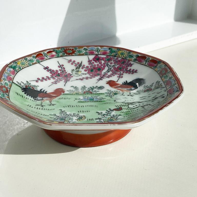 Beautiful chinoiserie footed vide poche or trinket dish. This piece would be fabulous for use as a trinket dish on a side table or nightstand. Its edges are octagonal and feature a scene of roosters and botanical decoration in the middle. Its footed