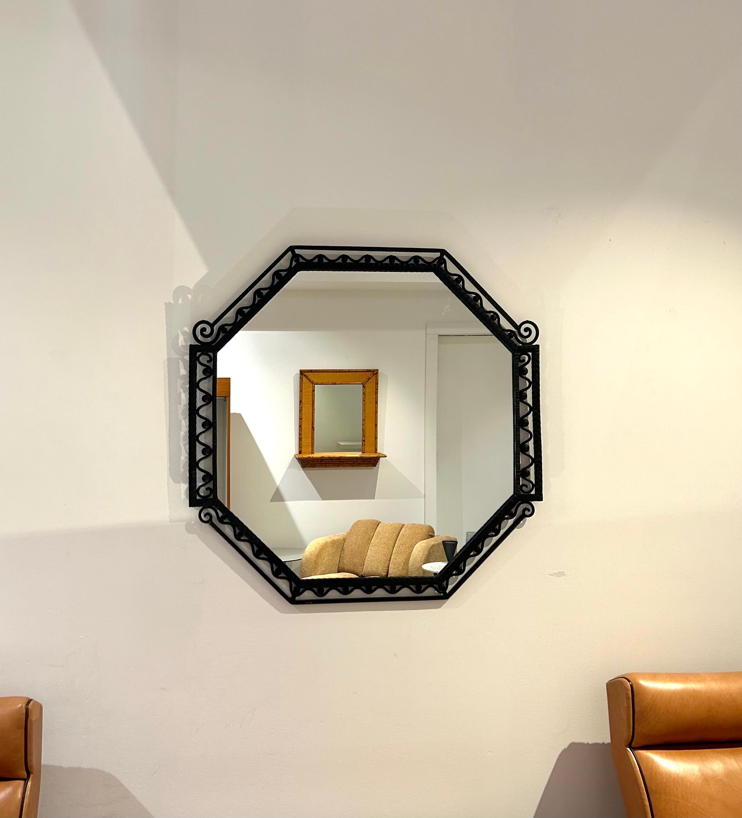 Miroir mural octogonal de style Art Deco dont le cadre en acier et en fer martelé noir est orné de vagues ondulantes, de rosettes et de spirales décoratives. Finition d'origine en très bon état et il n'y a pas de dommages ou de déformation dans le