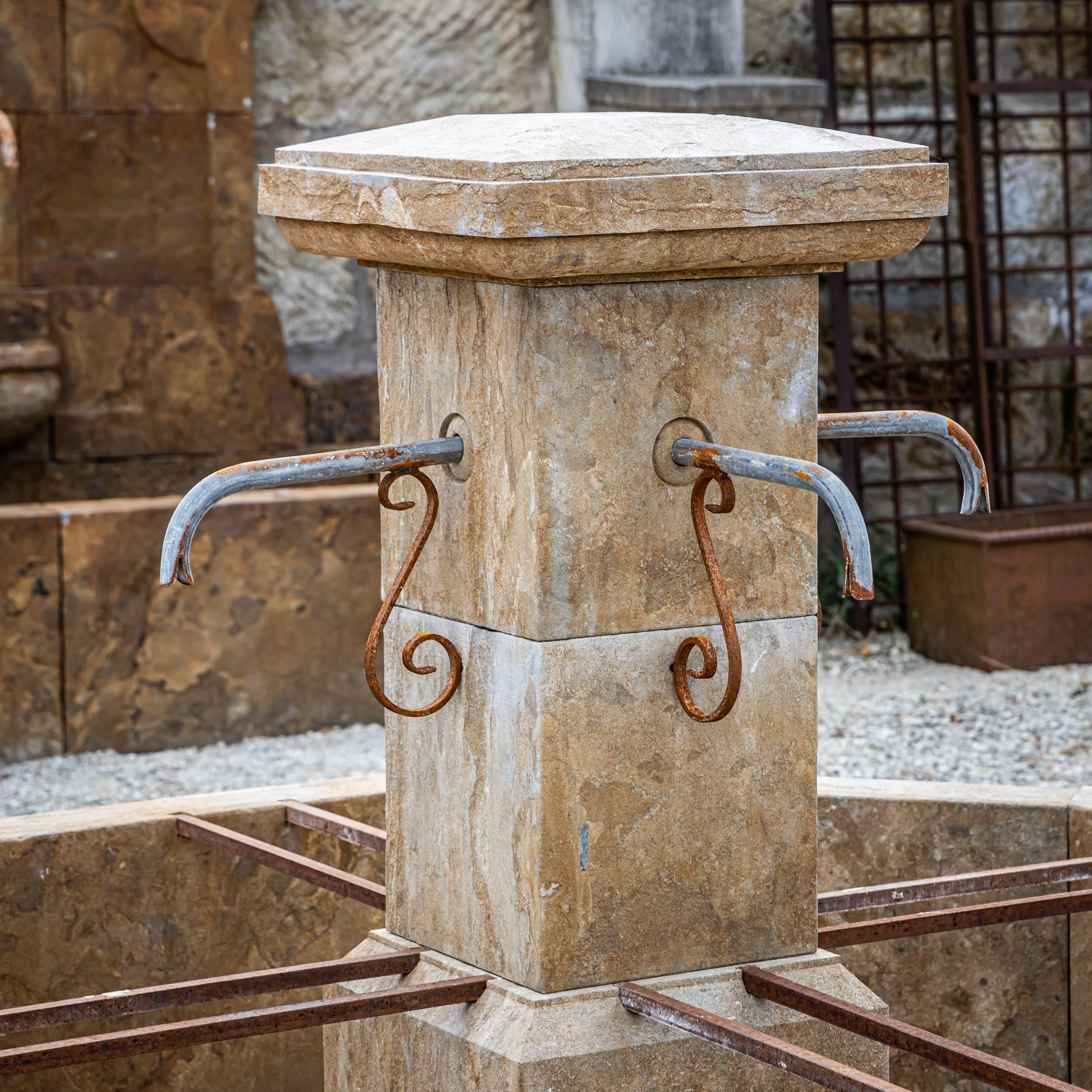 Fountain made of hand-chiseled, antique-patinated natural stone with an octagonal basin and four water spouts. The central column has a simple design, while internal iron reinforcements provide additional stability.