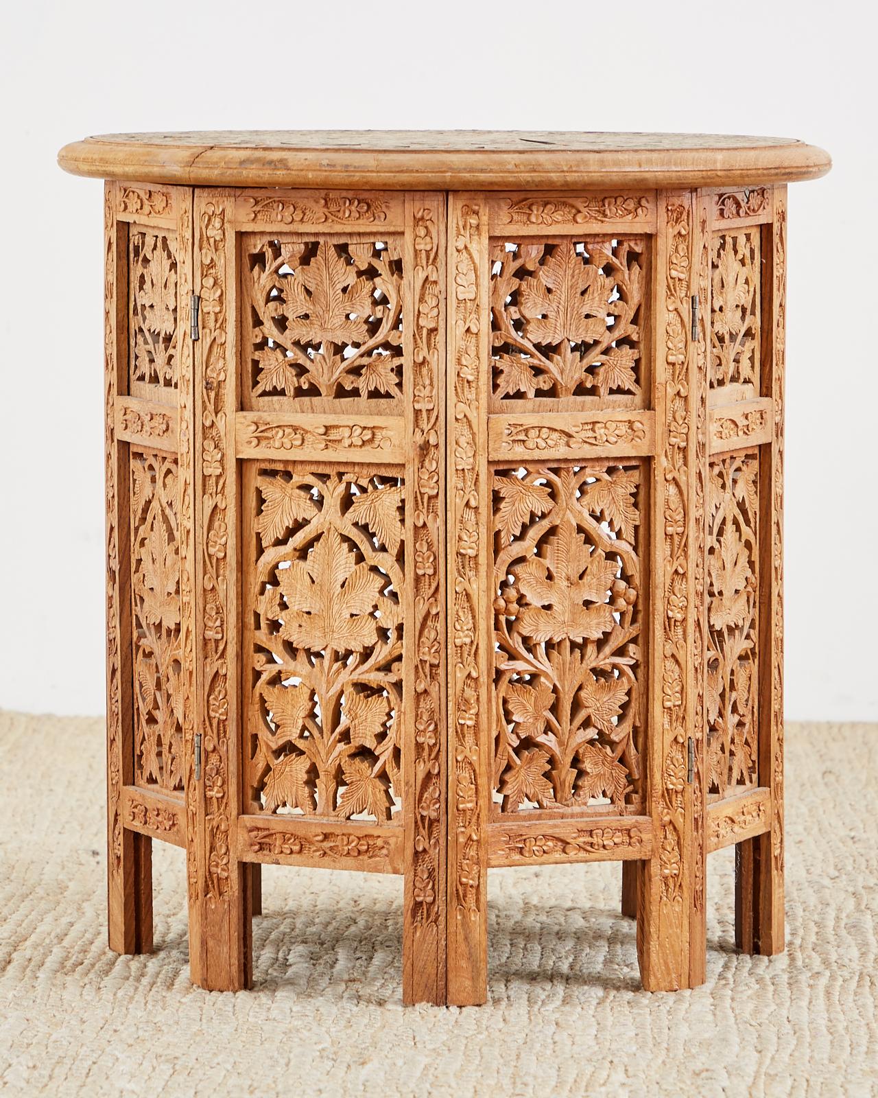 Octagonal carved teak tabouret style Moroccan side table or drinks table. Featuring foliate design piercings throughout base. The top of the table is round and has a small intricate floral motif mosaic inlay. The campaign style table top is