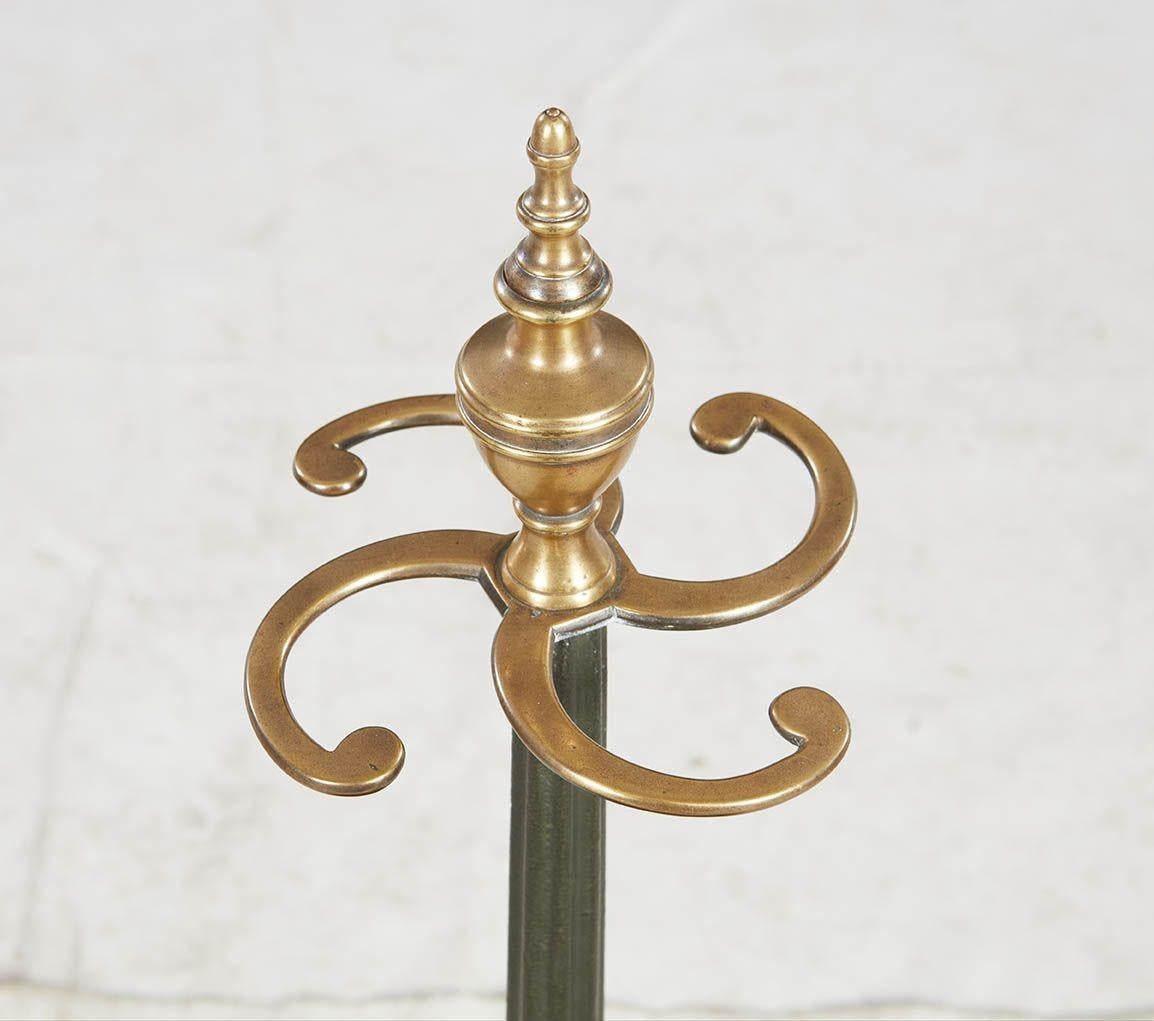 A sculptural umbrella stand in heavy iron with a brass top featuring four spiralled umbrella hooks under a finial, all mounted on a tapered and fluted iron column fixed to a deep octagonal iron bowl supported on paw feet. Fine quality construction
