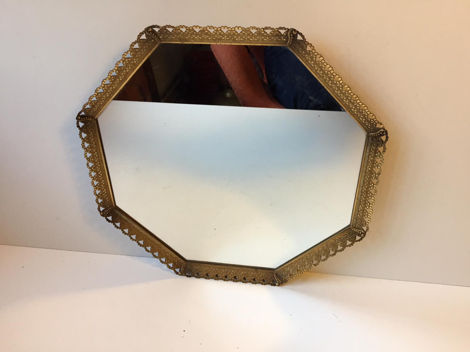 Wall-mounted or free standing octagonal vanity mirror. It features a partially pierced and ornamented brass frame. The mirror was manufactured in Denmark during the 1950s.