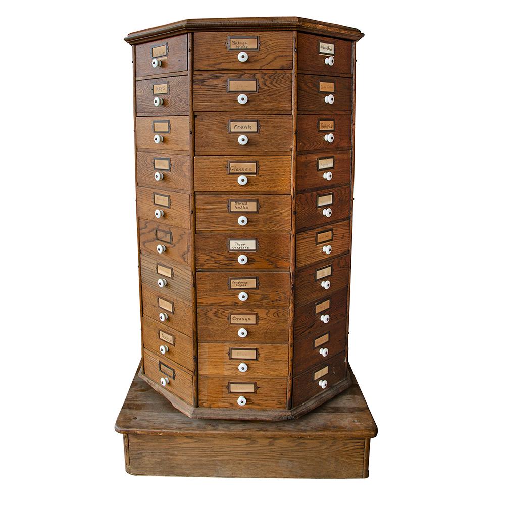 This early 20th century rotating hardware cabinet is a great piece of American industrial furniture. Set on a wooden box base, the cabinet has full 360-degree rotation with 80 triangular drawers, each fitted with a porcelain knob. The drawers have