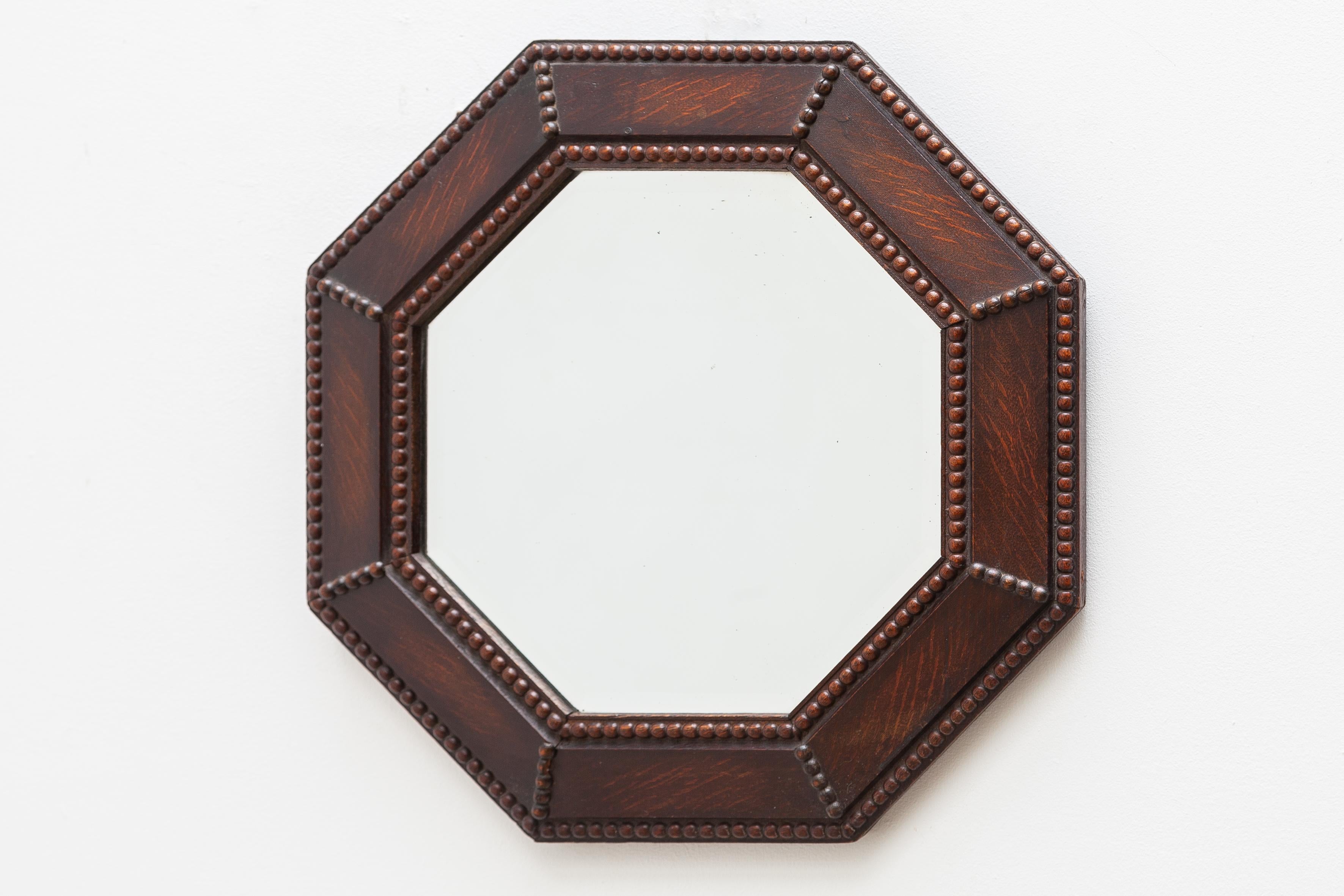 Very charming wall hanging octagonal oak framed beveled glass mirror in original good condition, designed in England, 1930s with beautiful decorative wood carvings around the frame.