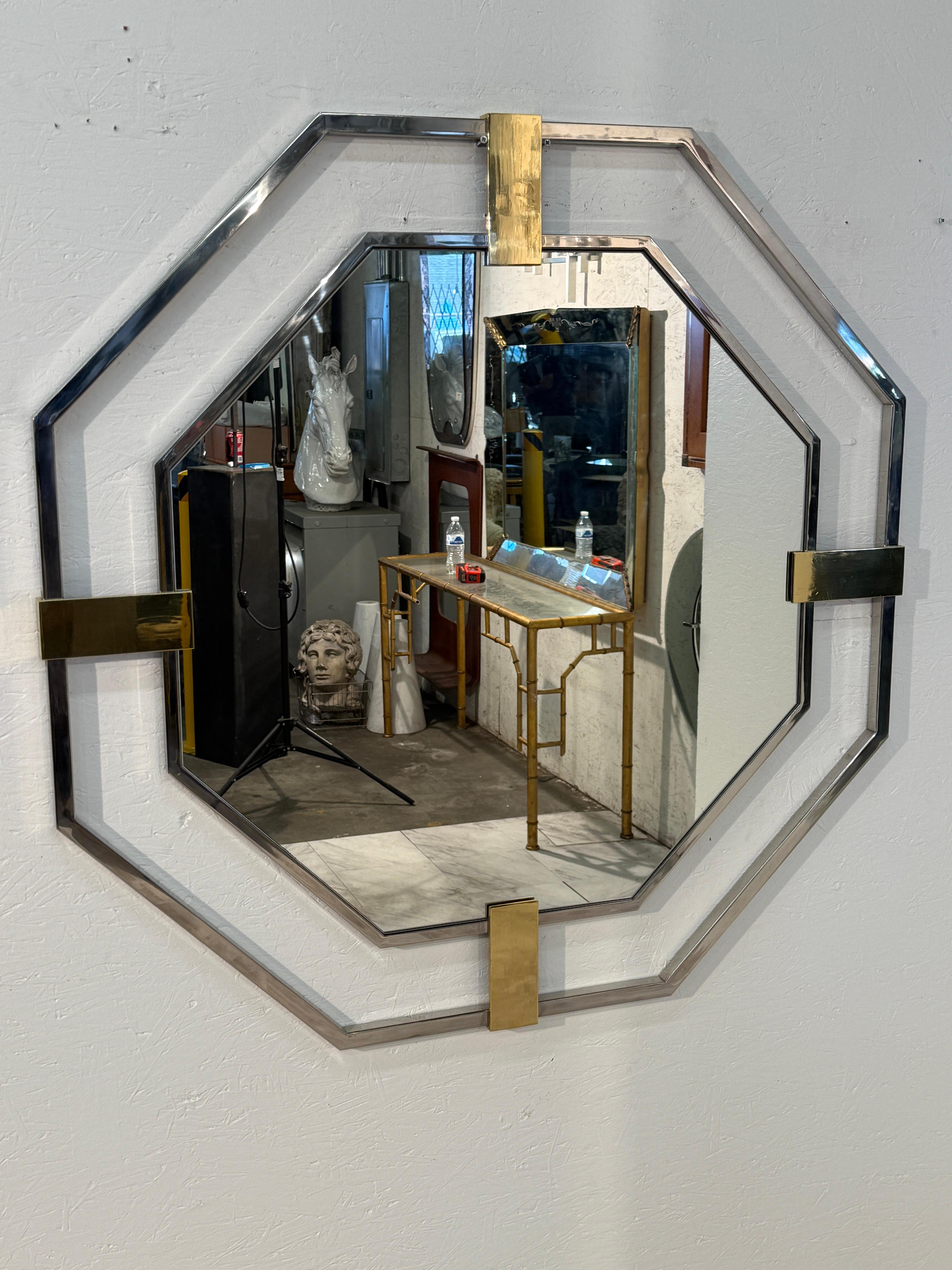 Un audace specchio da parete ottagonale italiano incorniciato in cromo lucido con sorprendenti supporti angolari in ottone. Il design geometrico evidenzia la qualità architettonica dello specchio, mentre il contrasto tra il cromo freddo e l'ottone