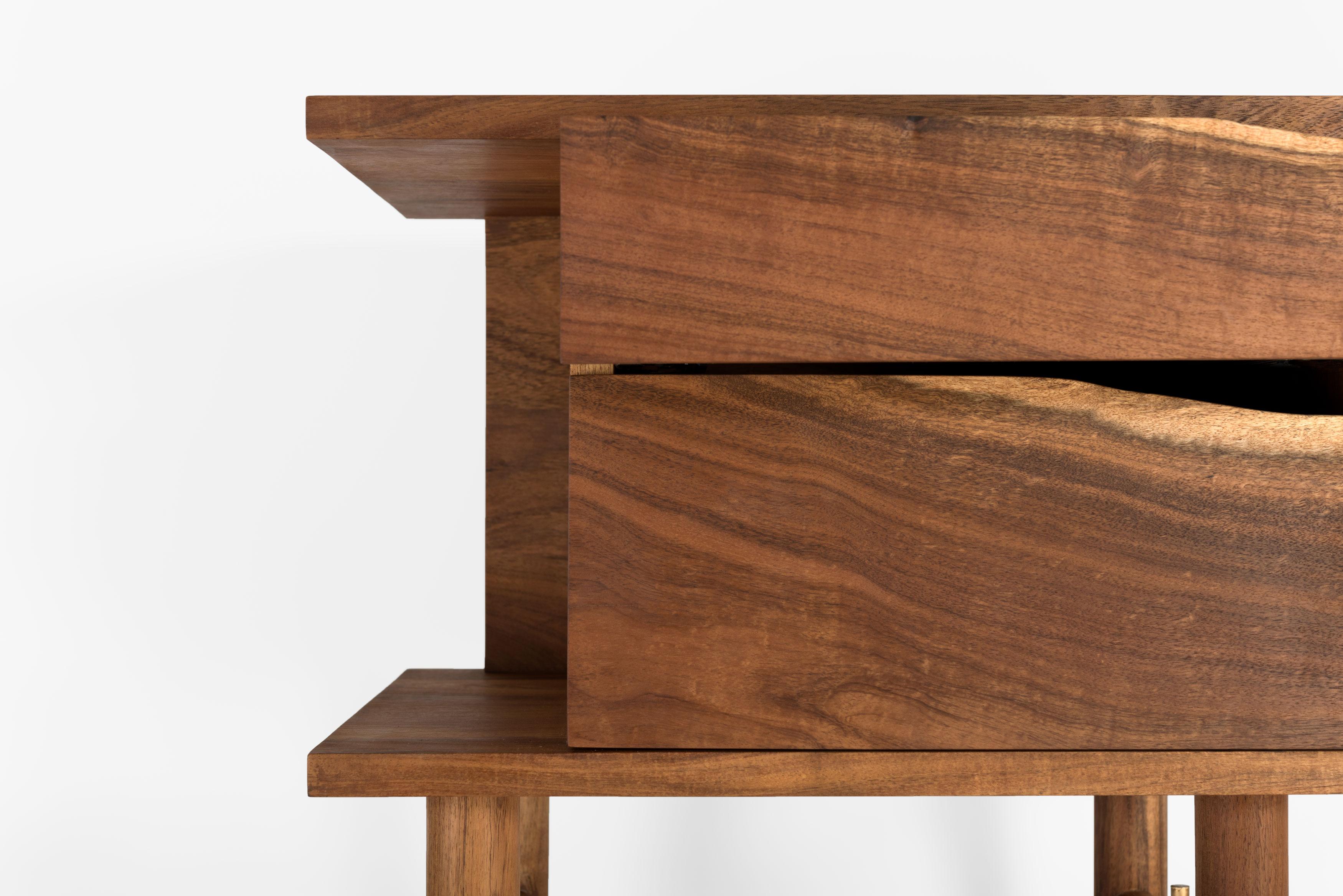 Le design de la table de nuit Ocum est caractérisé par la recherche de proportions équilibrées, la simplicité des formes de base et une construction minimaliste. Les textures contrastées du noyer des Caraïbes et les détails en bronze lui donnent