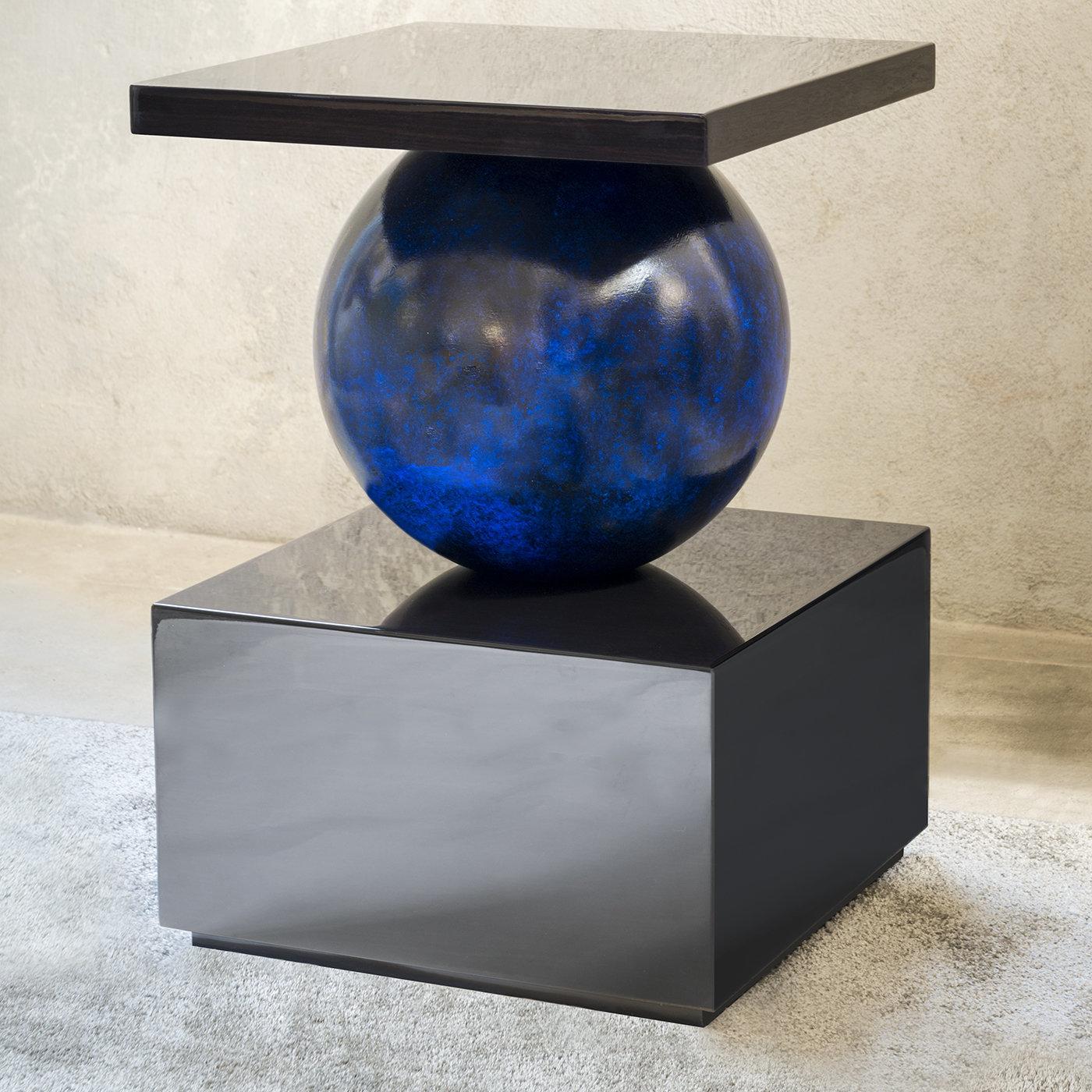 Cette étonnante table d'appoint est une œuvre d'art fonctionnelle, à la fois classique et avant-gardiste. La silhouette distinctive présente un corps sphérique bleu coincé entre un plateau de table carré et une base carrée solide, tous deux avec une