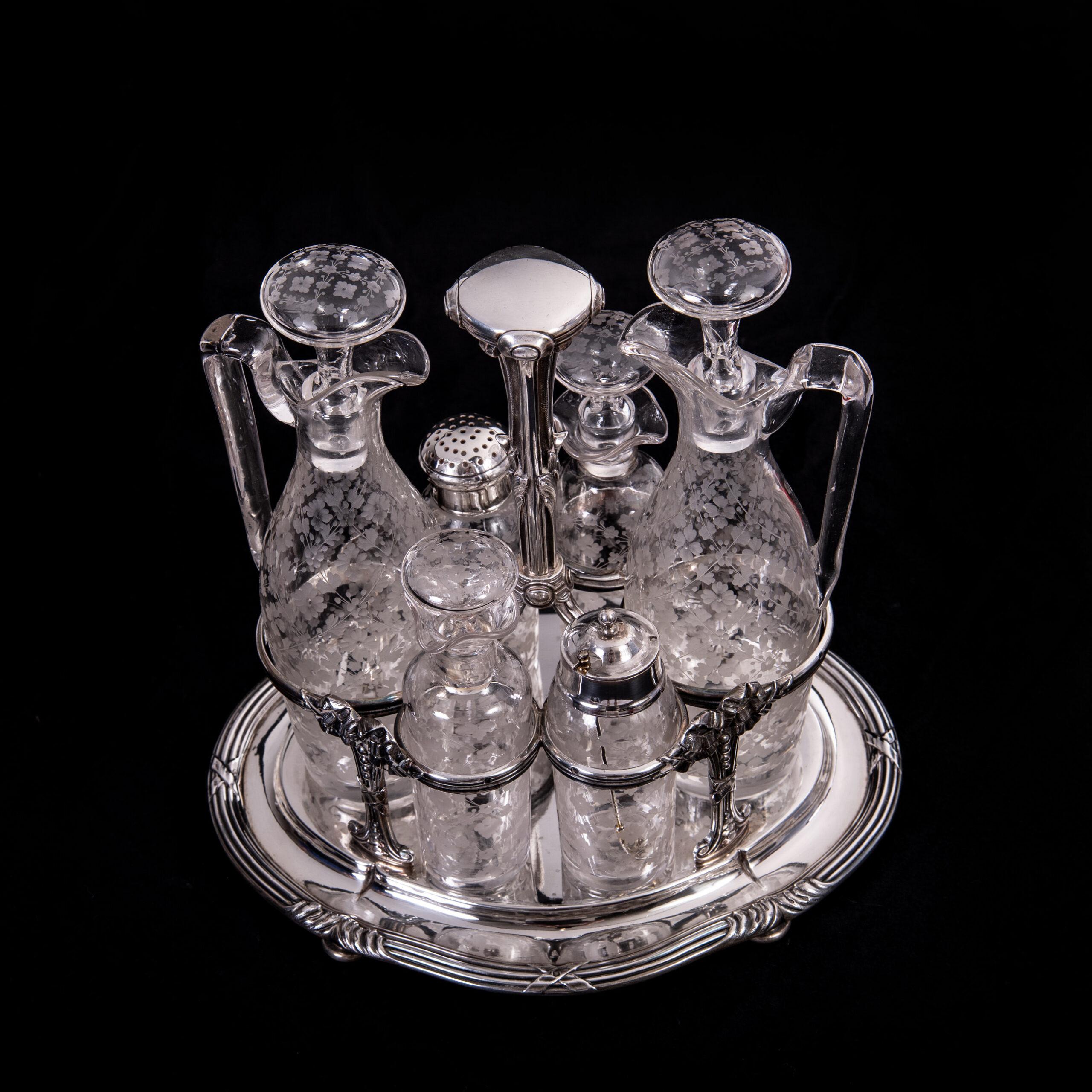 Odiot Paris 900/- silver cruet

oval stand with cross-band decoration, with 4 feet and central handle, around which are grouped holders for the glass inserts.

These consist of 2 jugs with spouts and stoppers, 2 small bottles with stoppers, a shaker