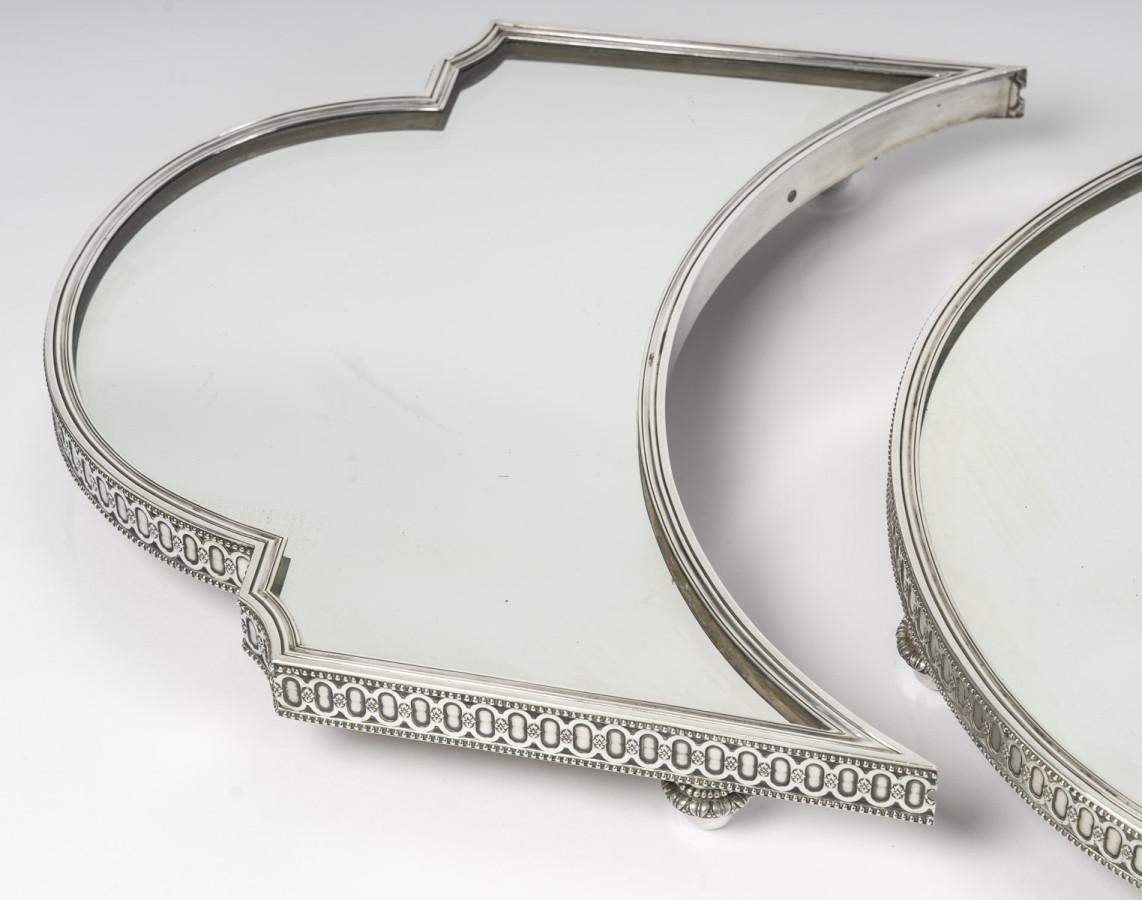Impressive three-piece centerpiece with mirrored bases on an oak parquet floor, surrounded by a solid silver ingot mold decorated with ovals and a row of fine pearls, mounted on spinning top feet. The oval centerpiece is completed by two sections