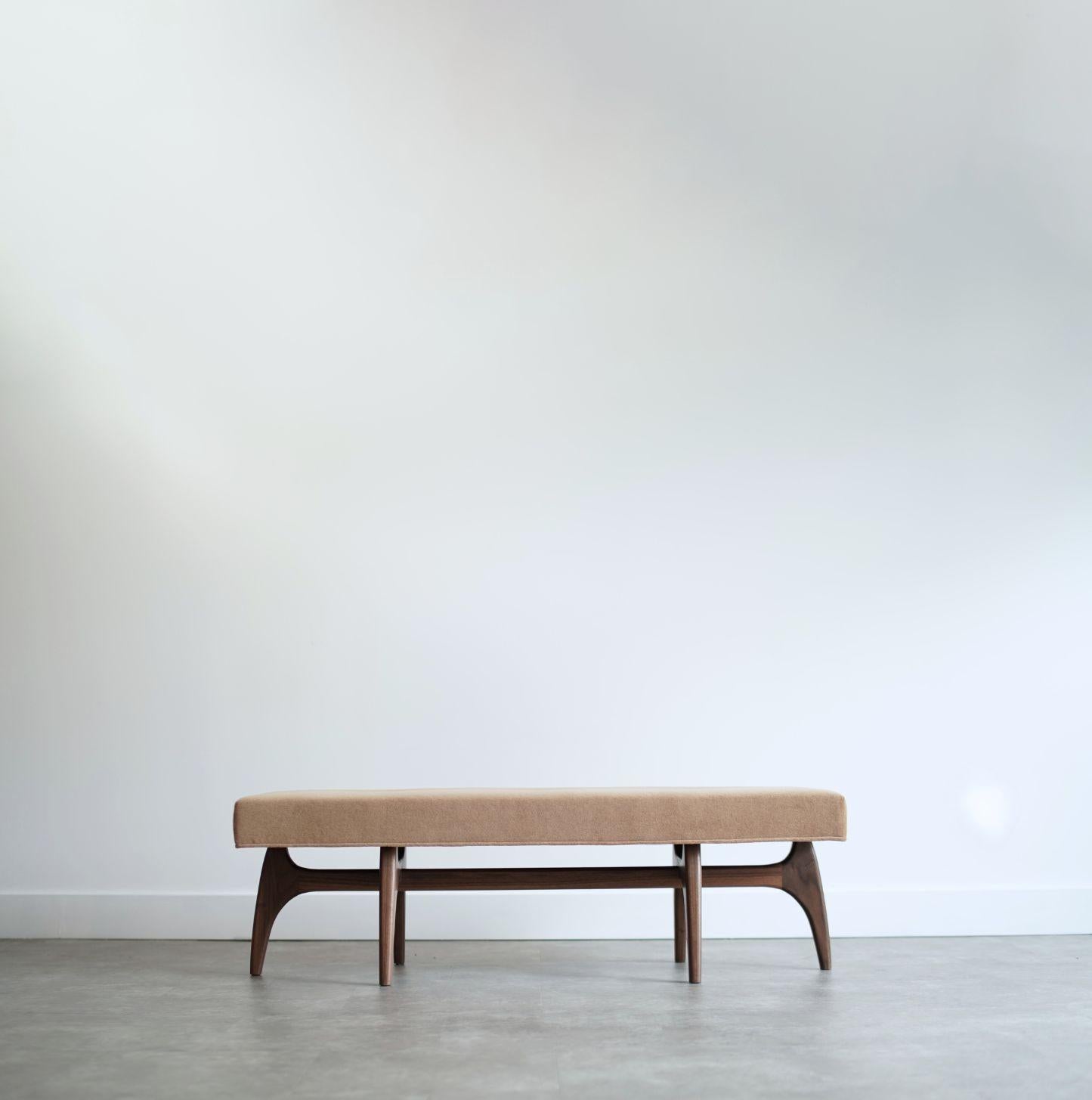 Artísticamente equilibrado y fabricado a mano, este banco combina una estética ligera con una sólida construcción. El cojín rectangular descansa sobre una escultural base de madera con elegantes curvas inclinadas inspiradas en el diseño moderno de