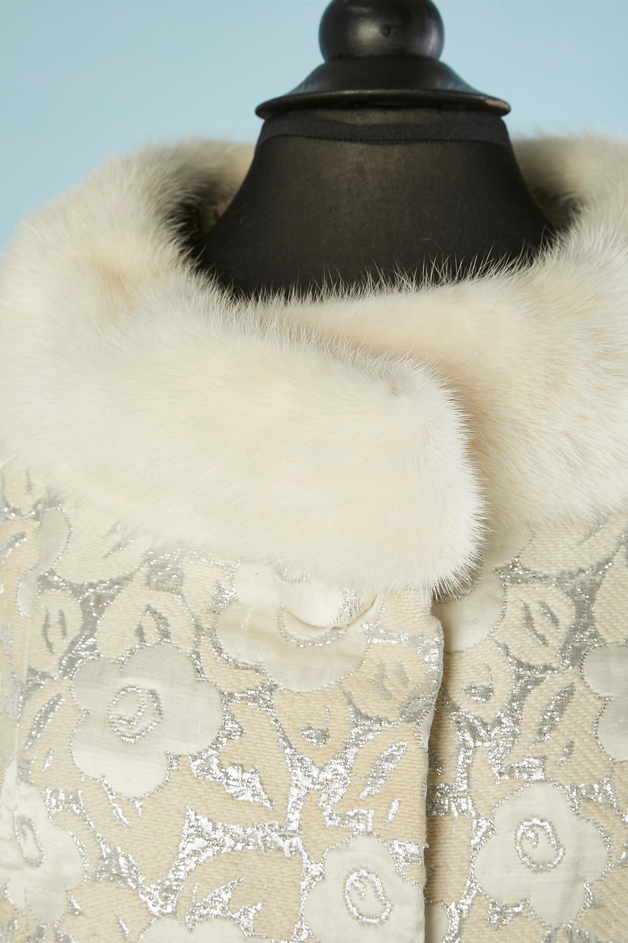 Cappotto monopetto in damasco bianco sporco e argento con collo in visone. La fodera è probabilmente in acetato o rayon. 2 bottoni rivestiti con lo stesso tessuto sulla parte centrale del davanti. Scatto nascosto. Tasca su entrambi i lati. 
TAGLIA