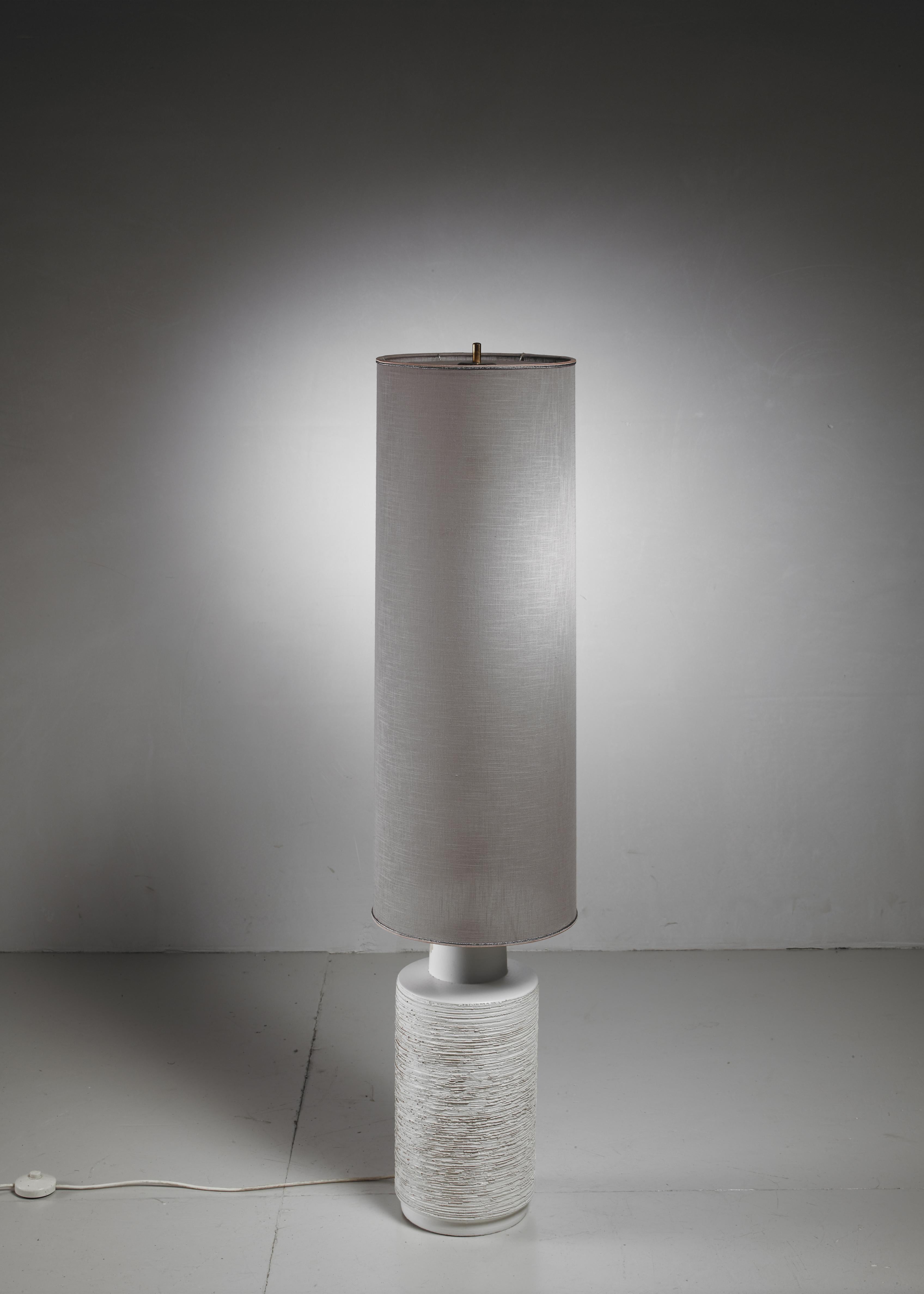 Eine Stehlampe aus cremefarbener Keramik mit einem großen, zylindrischen, grauen Leinenschirm.