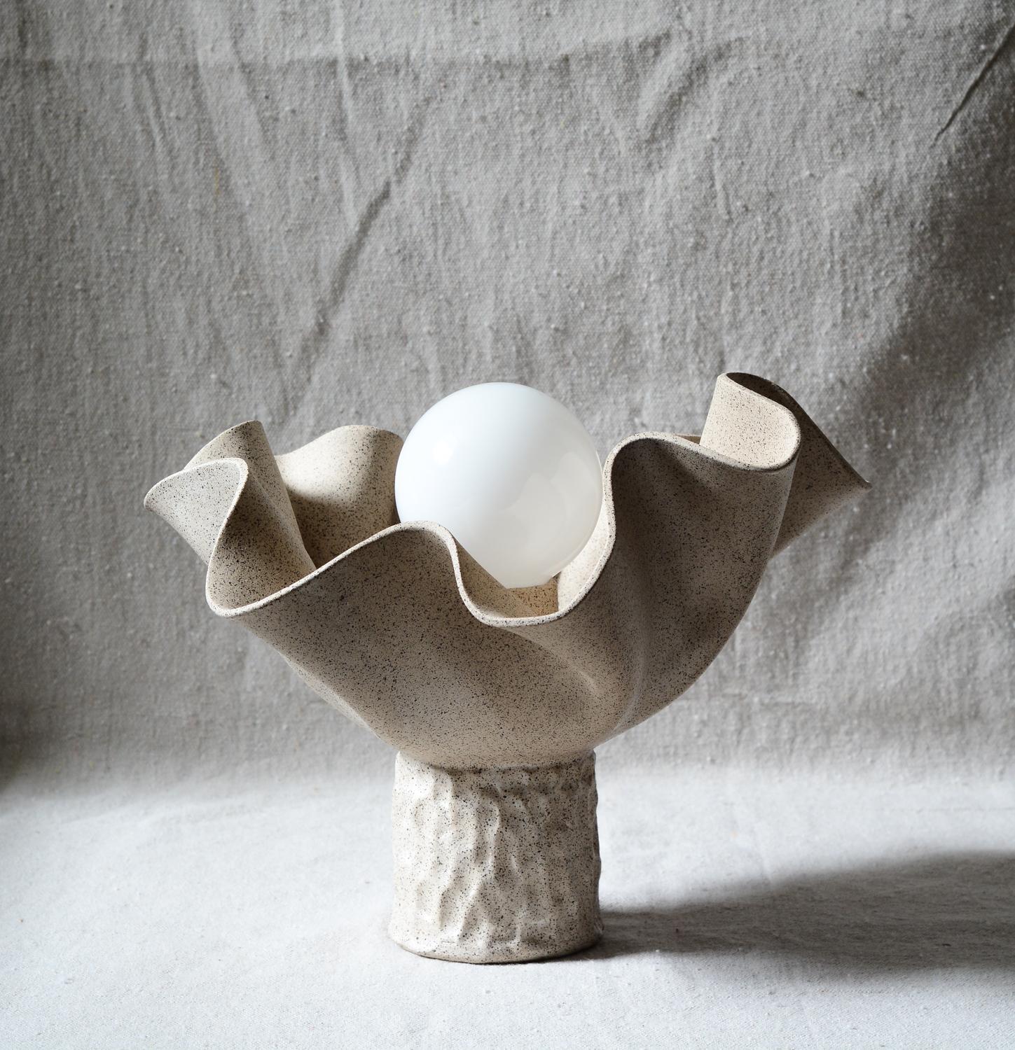 Handbuilt folded stoneware clay table lamp inspired by nature's undulations and fabric evokes a sense of organic beauty and tactile elegance. 
The lamp embraces the organic, fluid shapes found in nature, with undulating curves and folds reminiscent