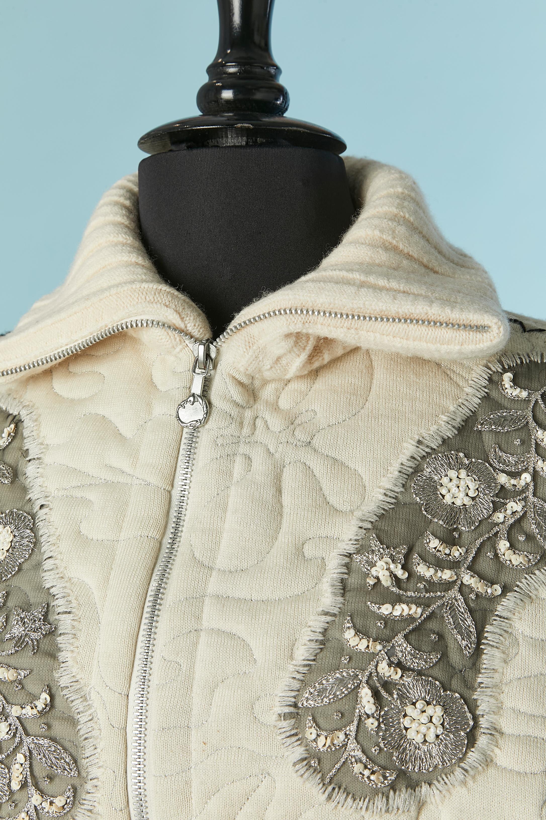 Giacca in maglia imbottita di colore bianco sporco con ricami in lurex, paillettes e perline. Composizione del tessuto principale: 100% lana. Fodera con motivo leopardato: 100% poliestere.
Cuciture superiori in lurex.
Chiusura con zip al centro