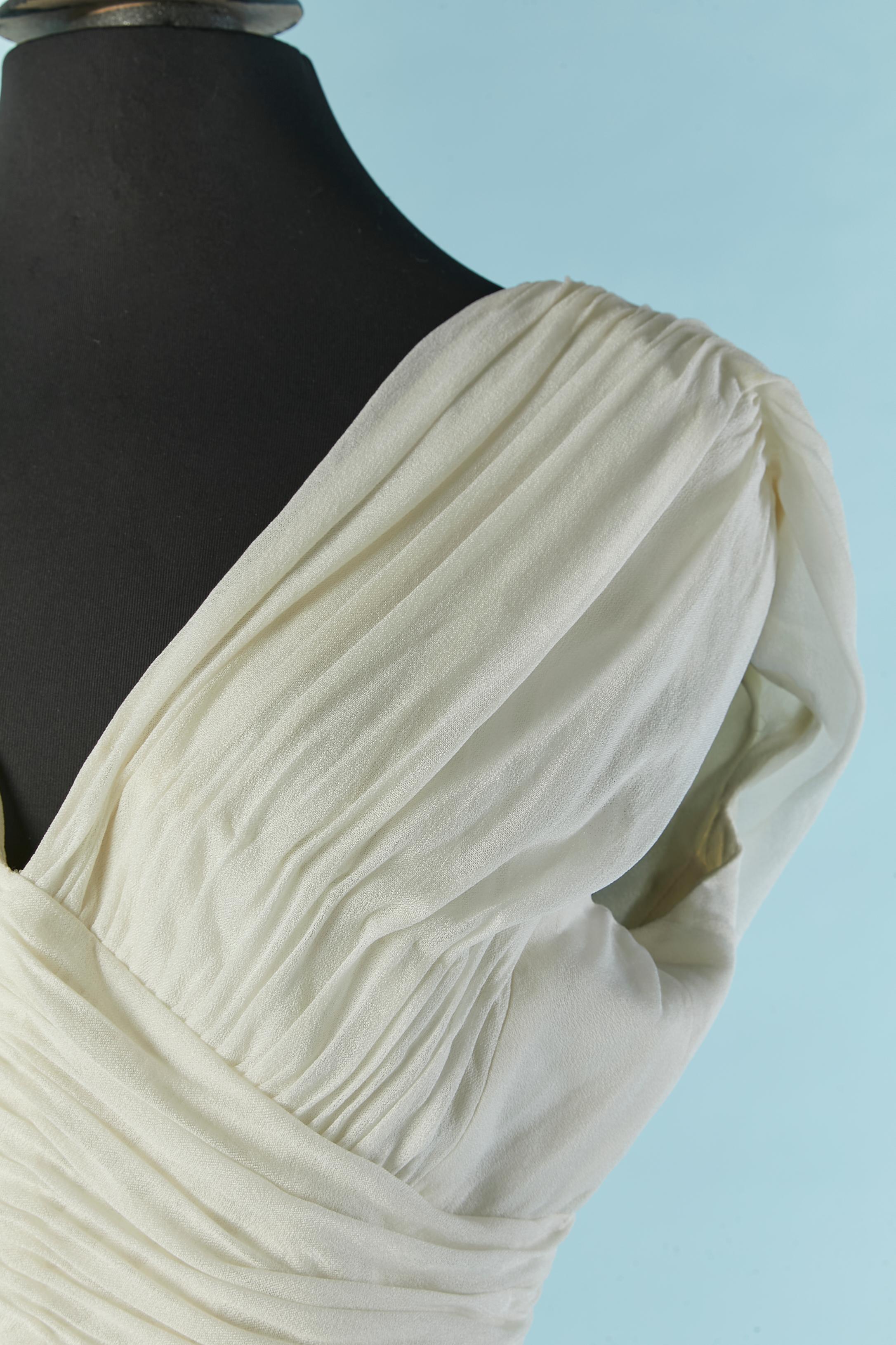 Abito da cocktail in jersey di seta bianco sporco, plissettato, avvolto e drappeggiato. Fascia in vita in gros-grain con chiusura a gancio sulla parte centrale della schiena. Chiusura con zip sul vestito al centro della schiena. Fodera in