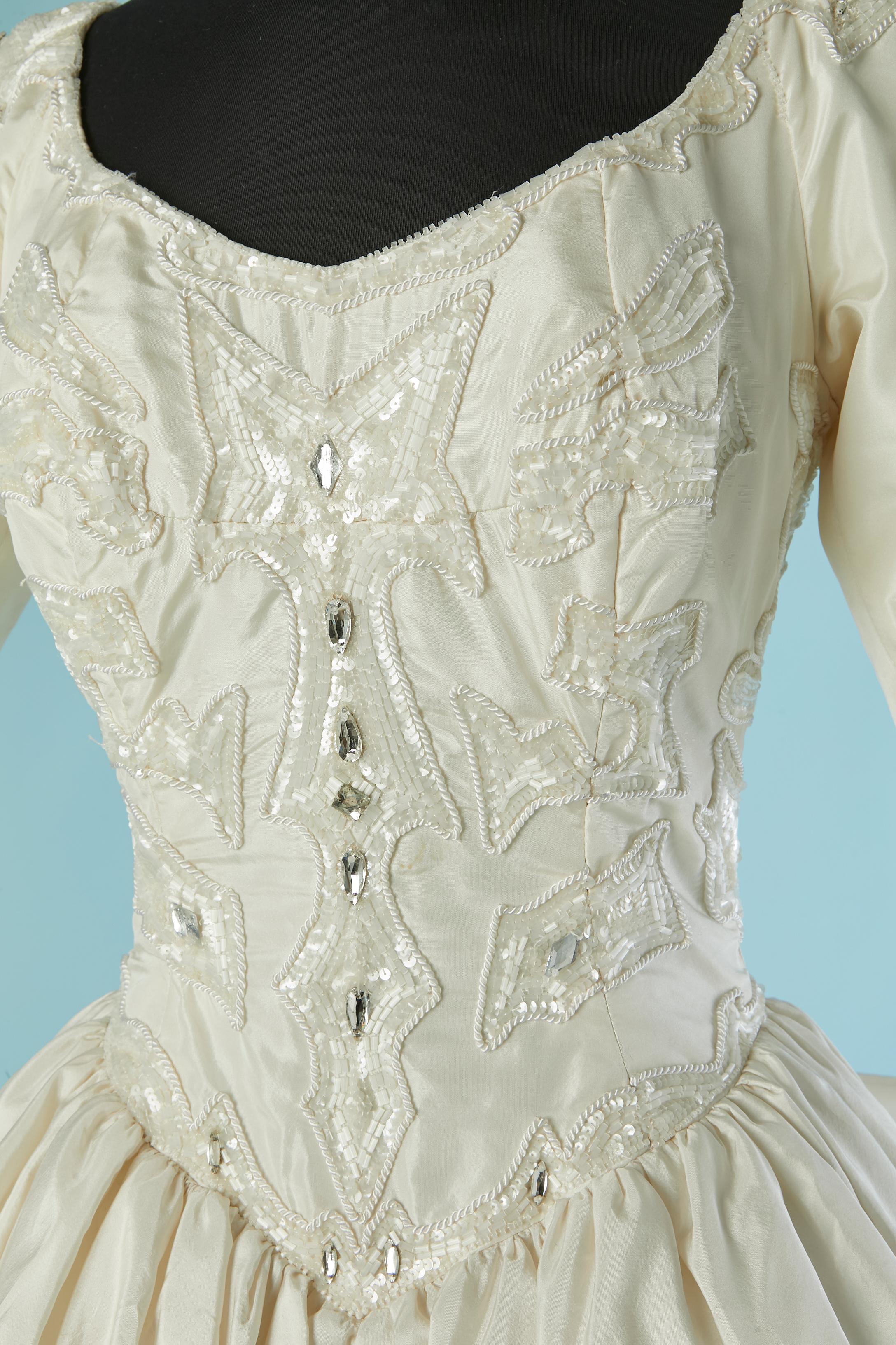 Abito da sposa in seta bianco sporco con perline. Disossato. Fodera in tulle. Chiusura con zip al centro della schiena. Reggiseno con ferretto all'interno dell'abito con chiusura a gancetto regolabile sulla parte centrale della schiena. 
TAGLIA