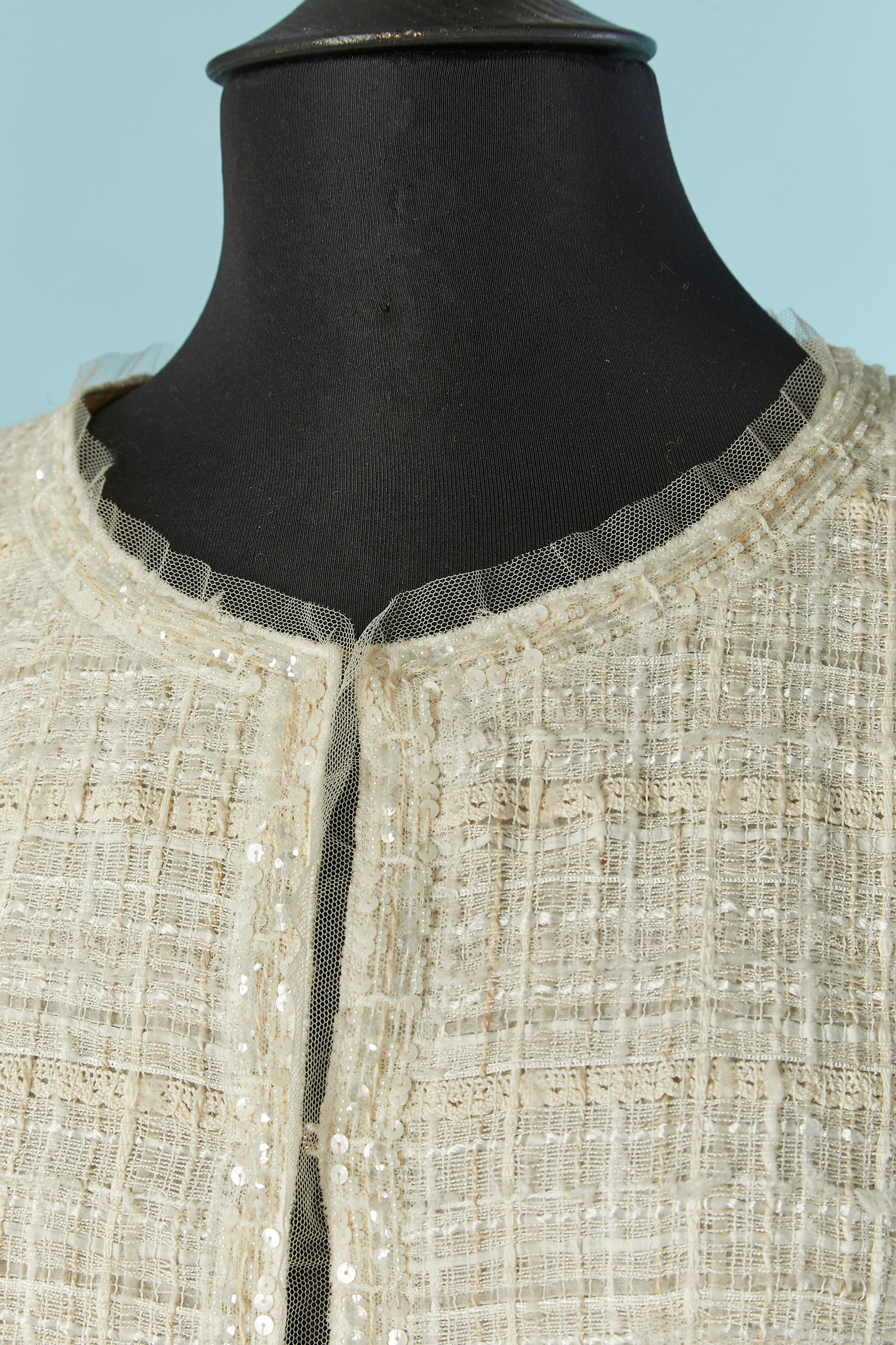 Off-white gewebte Jacke mit Perlen und Paillettenverzierung. 
Zusammensetzung des Hauptgewebes: 31% Baumwolle, 28% Viskose, 25% Nylon, 8% Leinen, 8% Acryl. 
Seidenfutter. 
Haken- und Ösenverschluss in der vorderen Mitte. Kette auf der Innenseite der