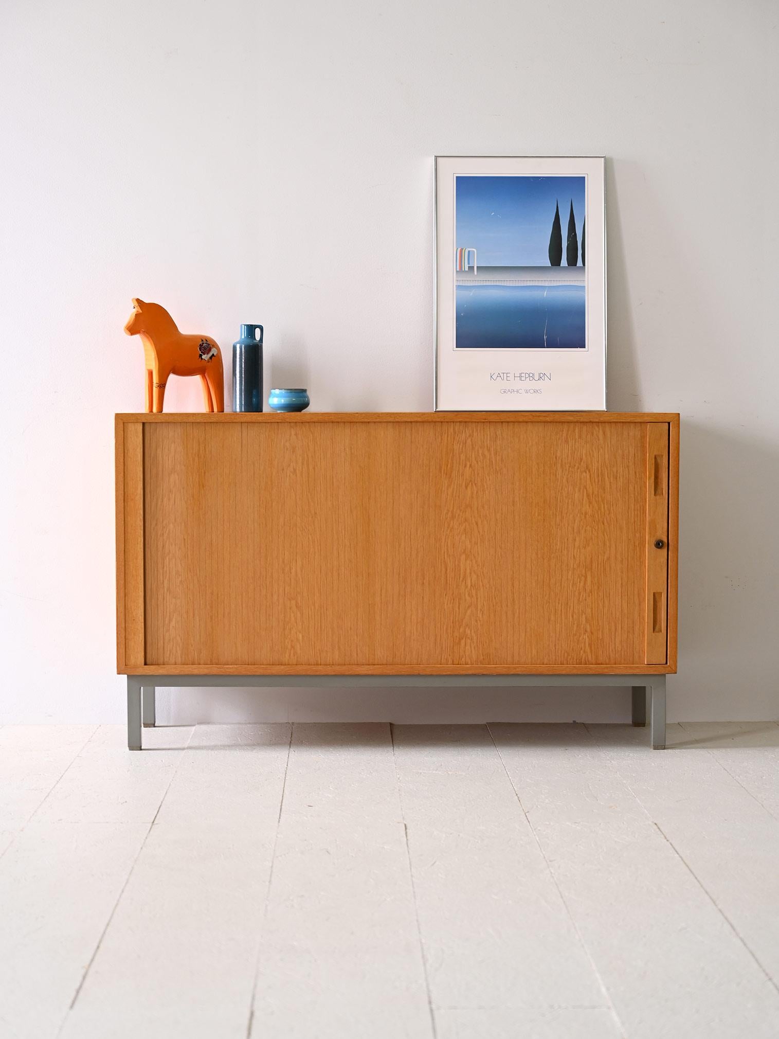 Oak sideboard cabinet with sliding door and metal feet.
 
The sliding door conceals a large compartment divided into two parts, the right one has seven wooden drawers while the left one has a large storage compartment with shelf.

Ideal for the room