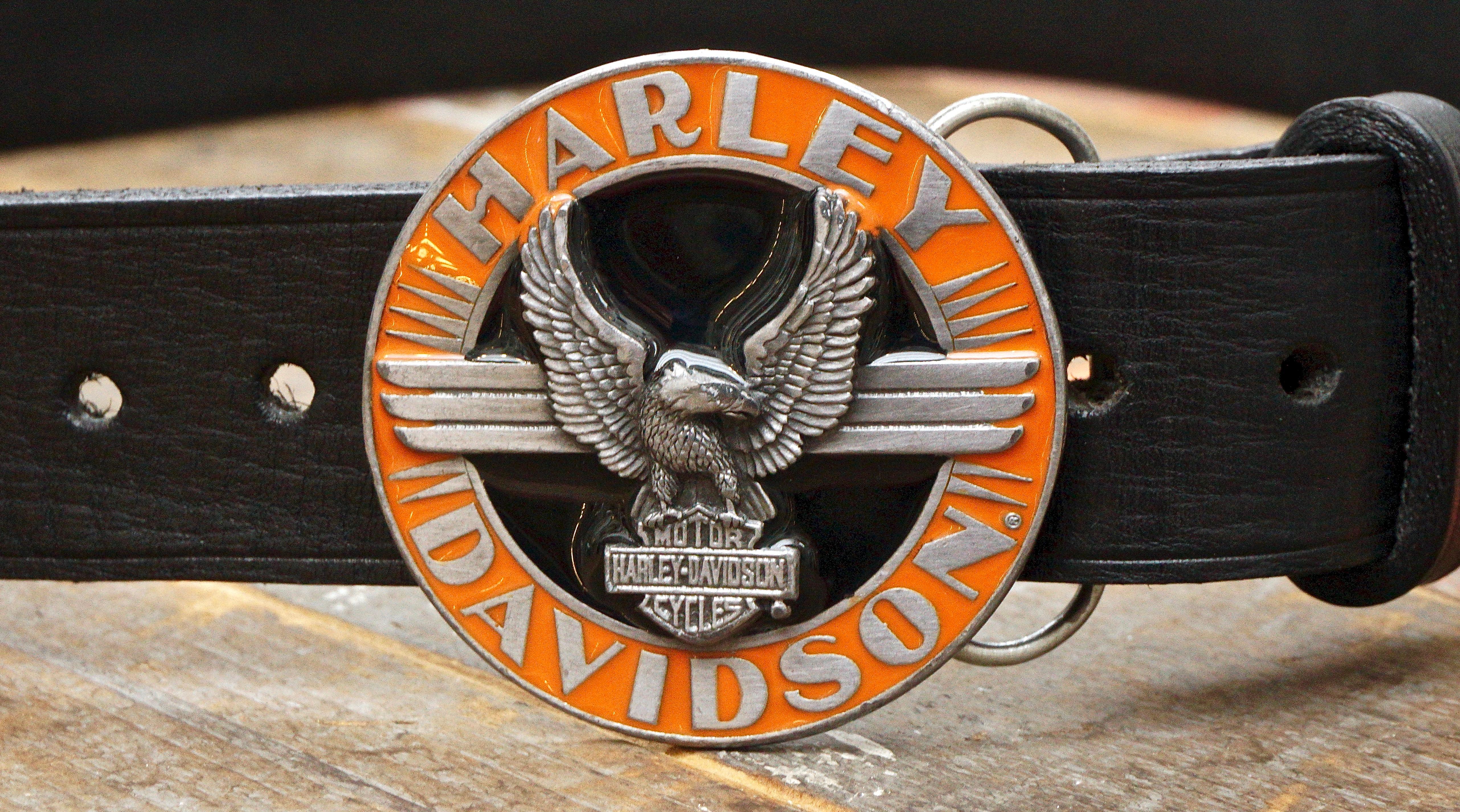 Official Harley Davidson thick black leather belt featuring the round orange and black enamel eagle buckle, circa 1992.  Measuring length (to the longest belt hole) 114.3cm / 45 inches by width 3.7cm / 1.45 inch and depth 4mm / .16 inch. The buckle