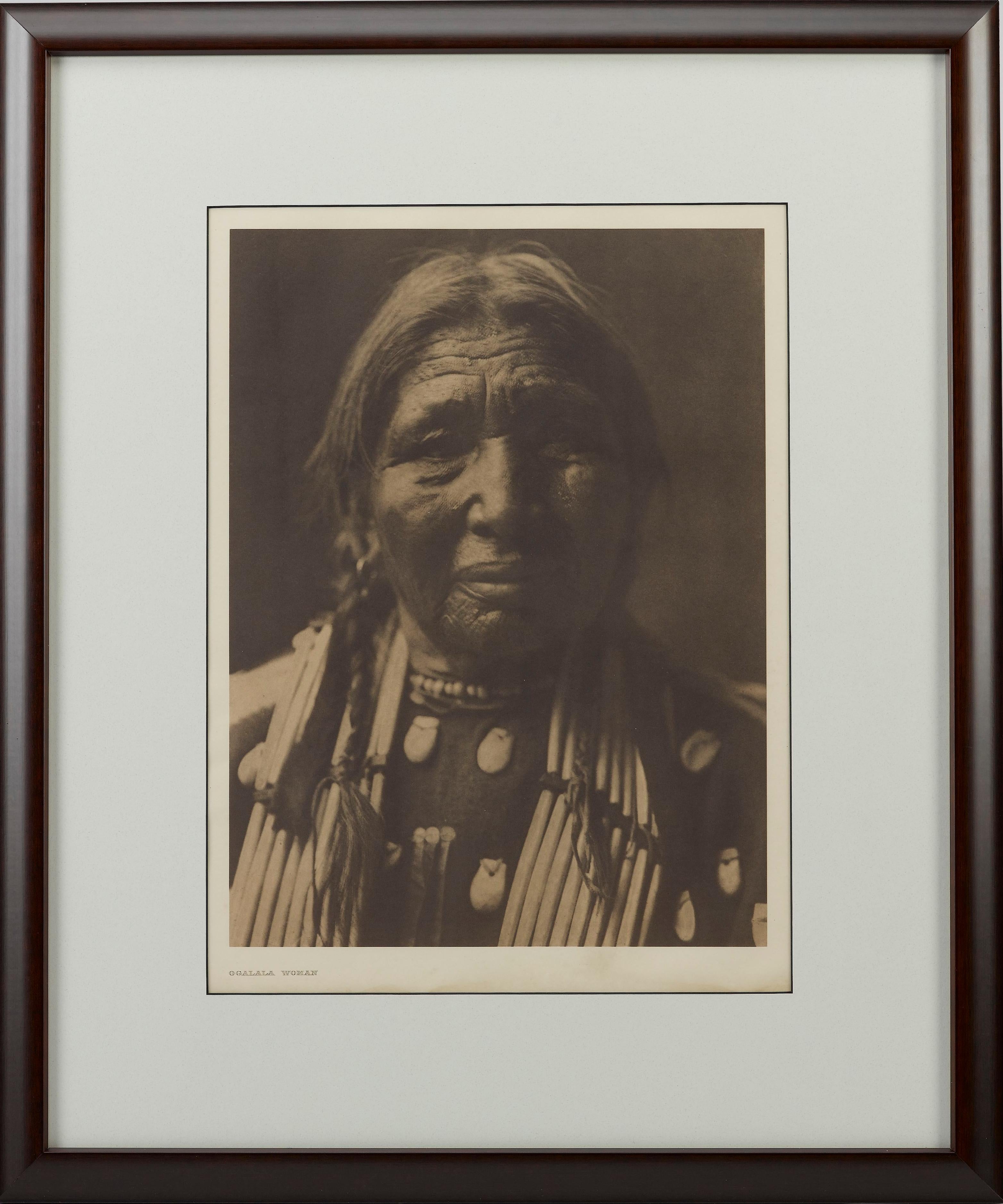 Presented is a fine photogravure portrait of an Ogalala woman by Edward Curtis. The image is Plate 94 from Supplementary Portfolio 3 of Edward Curtis' epic project The North American Indian. The caption provided by Curtis for this image is “A face