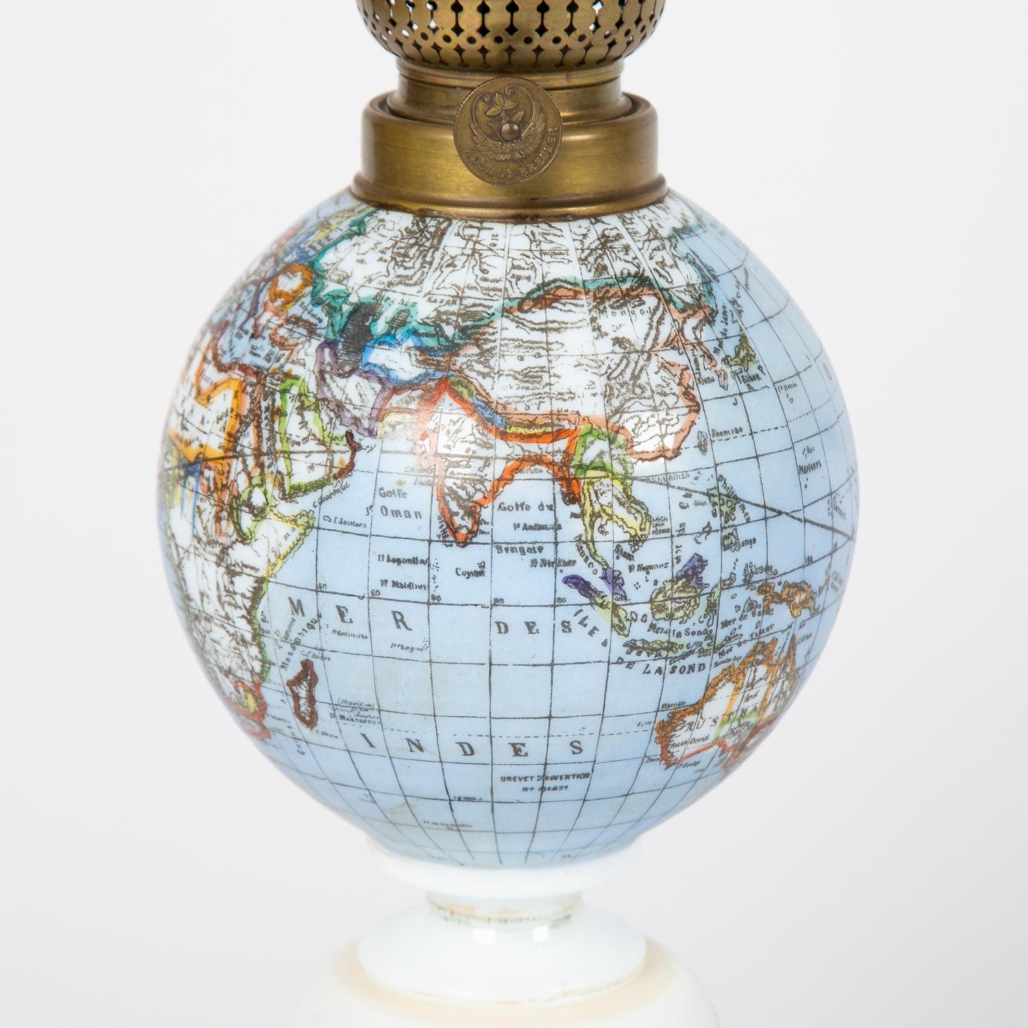 A rare late 19th century oil lamp with a globe shade and base decorated with a castle set in a rural scene, circa 1885.

Northern European for the French market. The countries and seas indicated on the globe written in French. 

Burner made by