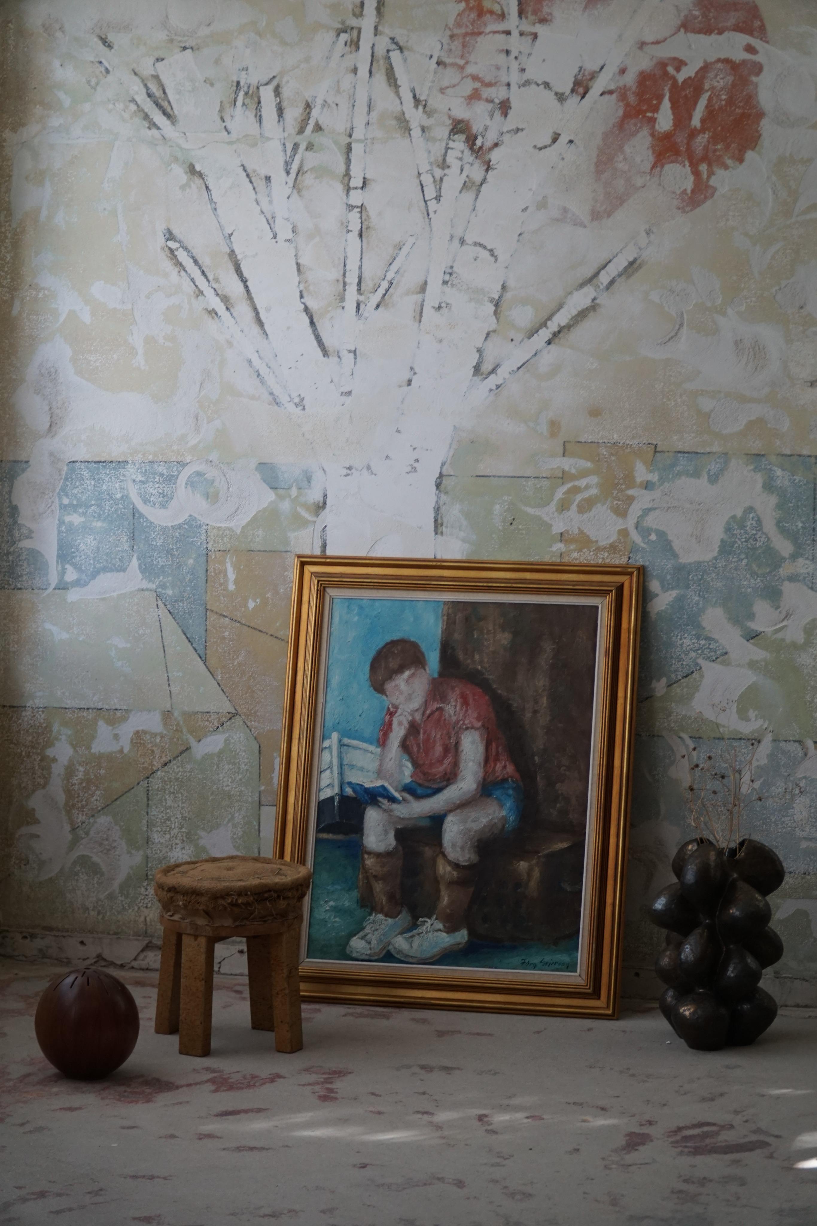 Presenting an enchanting oil painting by the Danish artist Jørgen Sejersen, made in between 1960-1980s. 
This particular artwork captures a peaceful scene, showcasing a young boy immersed in the interesting world of literature, resting a top a