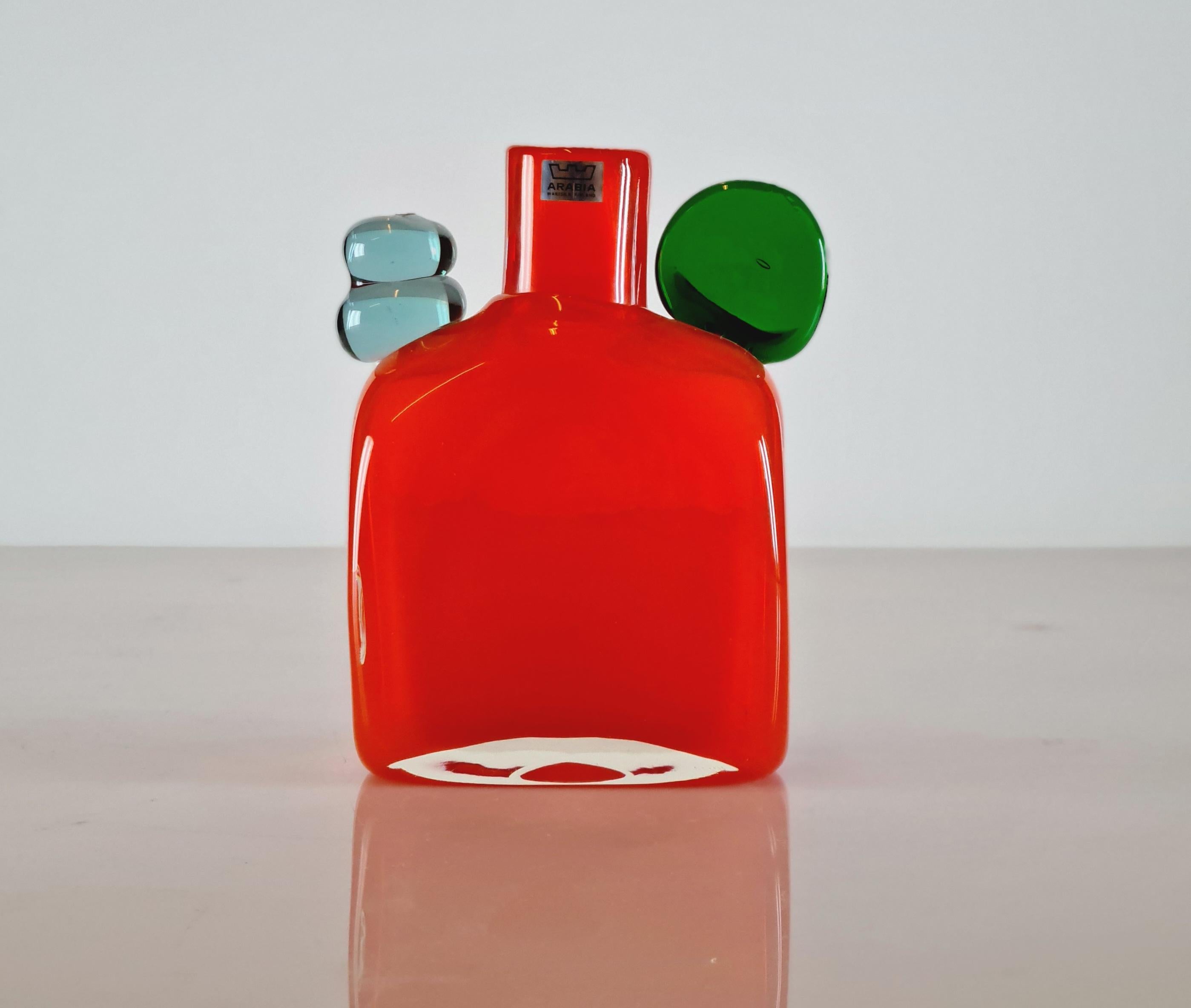 Diese leuchtend orangefarbene Pampula-Flasche mit grünen und hellblauen Details von Oiva Toikka ist eine perfekte Dekoration für sich allein. Der Gesamtzustand dieser spielerischen Kunst  Stück ist sehr gut und kommt mit der Oiva Toikka Nuutajärvi
