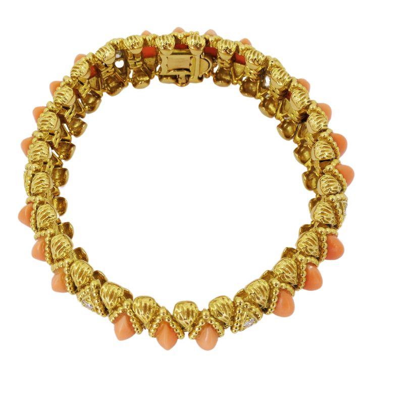 An exquisite coral and diamond bracelet by O.J. Perrin, crafted of 18k gold.
The bracelet is designed with a sequence of marquise shaped coral cabochons, each set within textured gold frames. Alternating between the coral settings are delicate