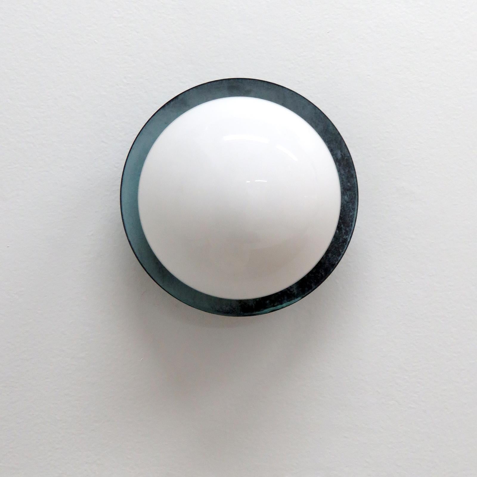 Splendida versione da esterno delle nostre applique Ojo disegnate da Gallery L7, realizzate e rifinite a mano a Los Angeles in ottone americano, con paralume centrale in vetro opalino su un disco in ottone con patina verde gris. Disponibile con