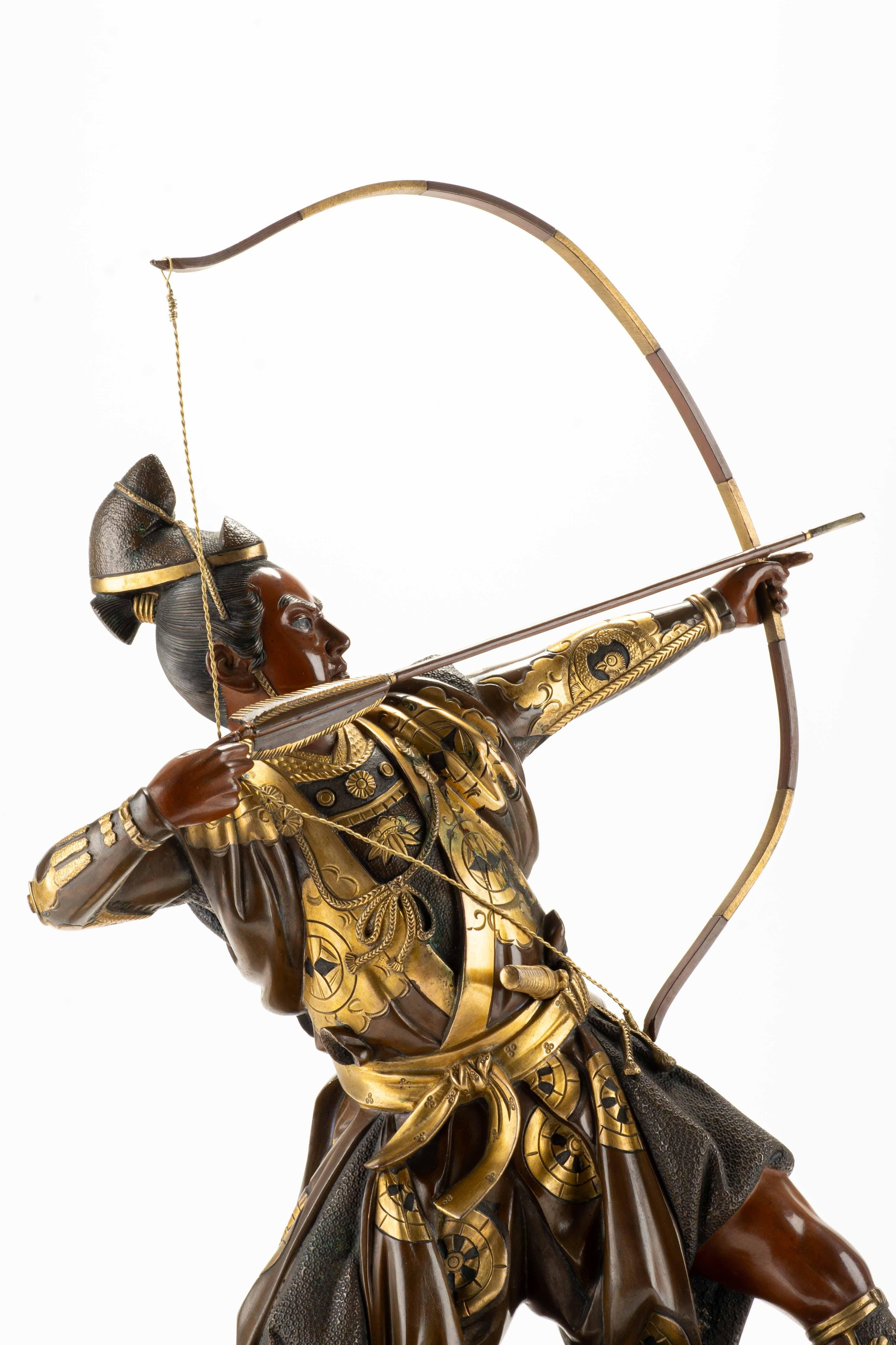 Sculpture en bronze patiné et doré représentant un archer samouraï agenouillé en train de tendre son arc. Le kimono est finement gravé et rehaussé de dorures qui contrastent avec la patine plus claire du corps.

La figurine repose sur un socle en