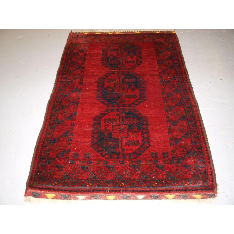 Alter afghanischer Dorfteppich in traditionellem Design mit drei großen Guls. Der Teppich ist von angenehmer roter Farbe mit dunklem Indigoblau, die Farbpalette ist insgesamt sehr weich und warm. Die Wolle hat einen wunderbaren Glanz und ist sehr