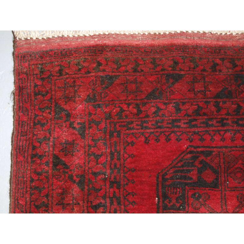 Alter afghanischer Dorfteppich mit traditionellem Design, der Teppich hat eine einzige Reihe von 3 großen afghanischen Guls.

Der Teppich hat eine ausgezeichnete mittelrote Farbe mit dunklem Indigoblau/Schwarz. Der Teppich hat an beiden Enden die