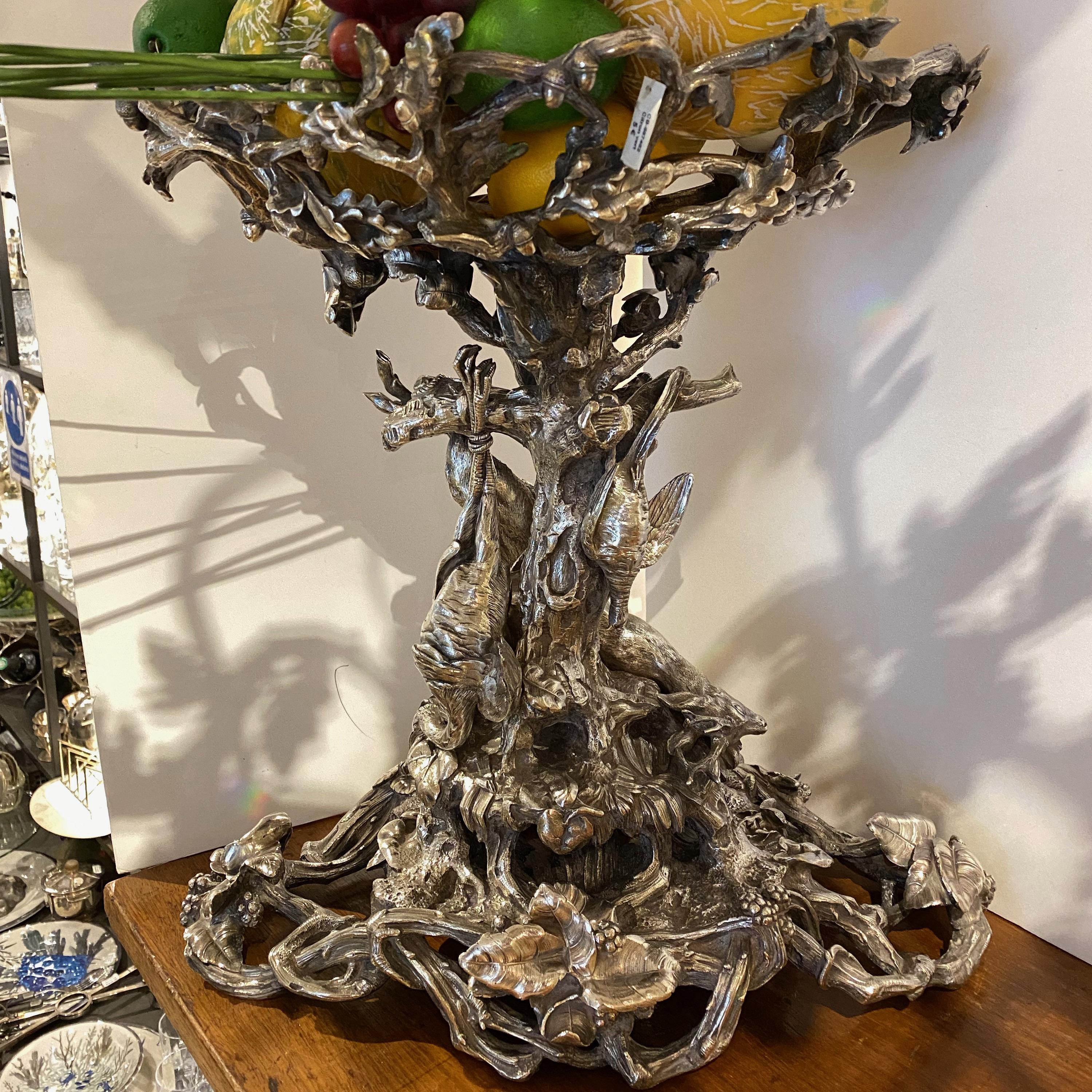 Ce centre de table signé Christofle est en bronze argenté avec une très belle patine, la partie artistique est un travail d'aboutissement, la base est percée composée de branches avec des feuilles et a des sculptures suspendues de gibier, oiseaux,